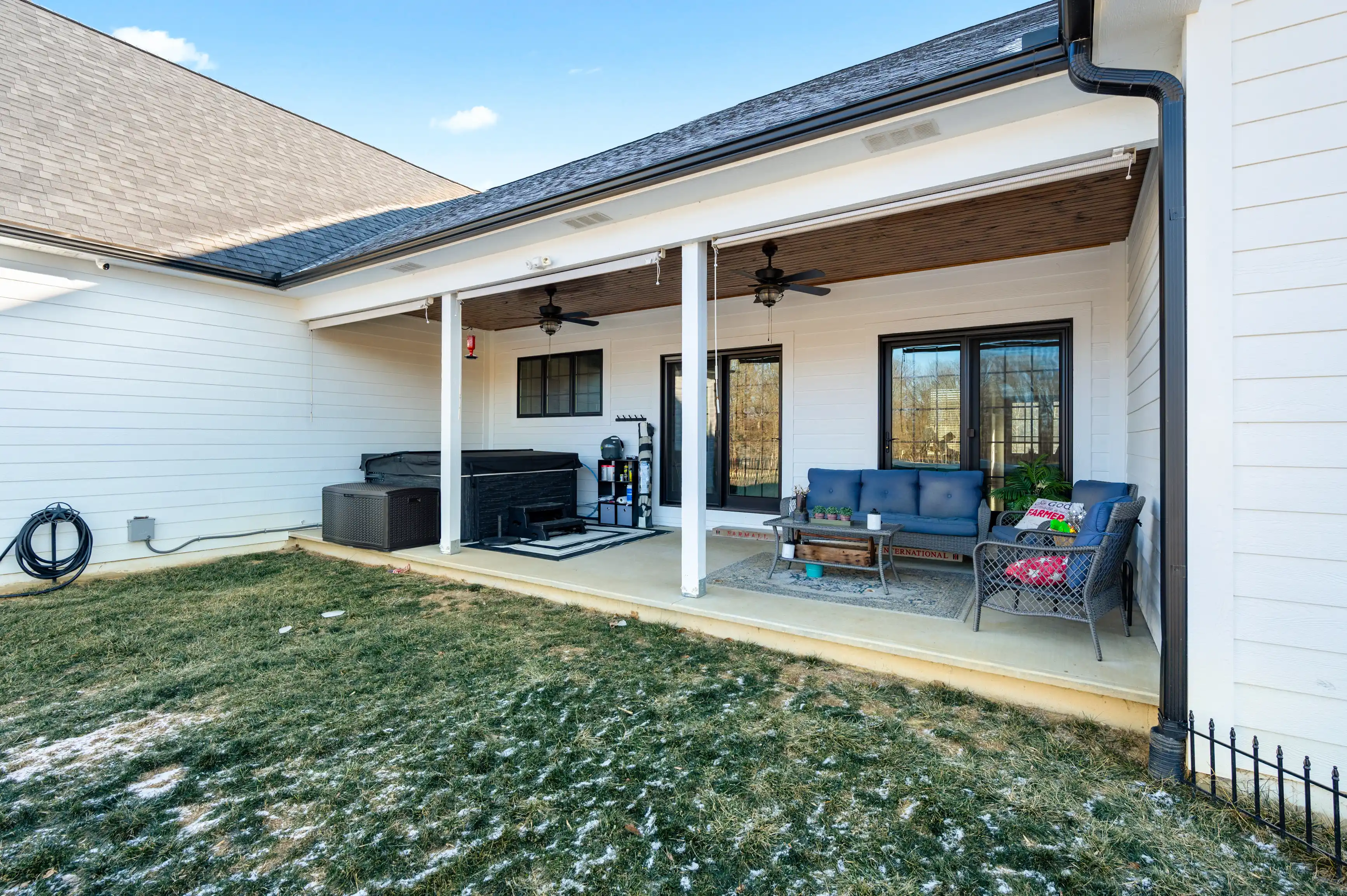 Backyard covered porch with seating area, grill, and ceiling fans attached to a house with a partially snow-covered lawn.