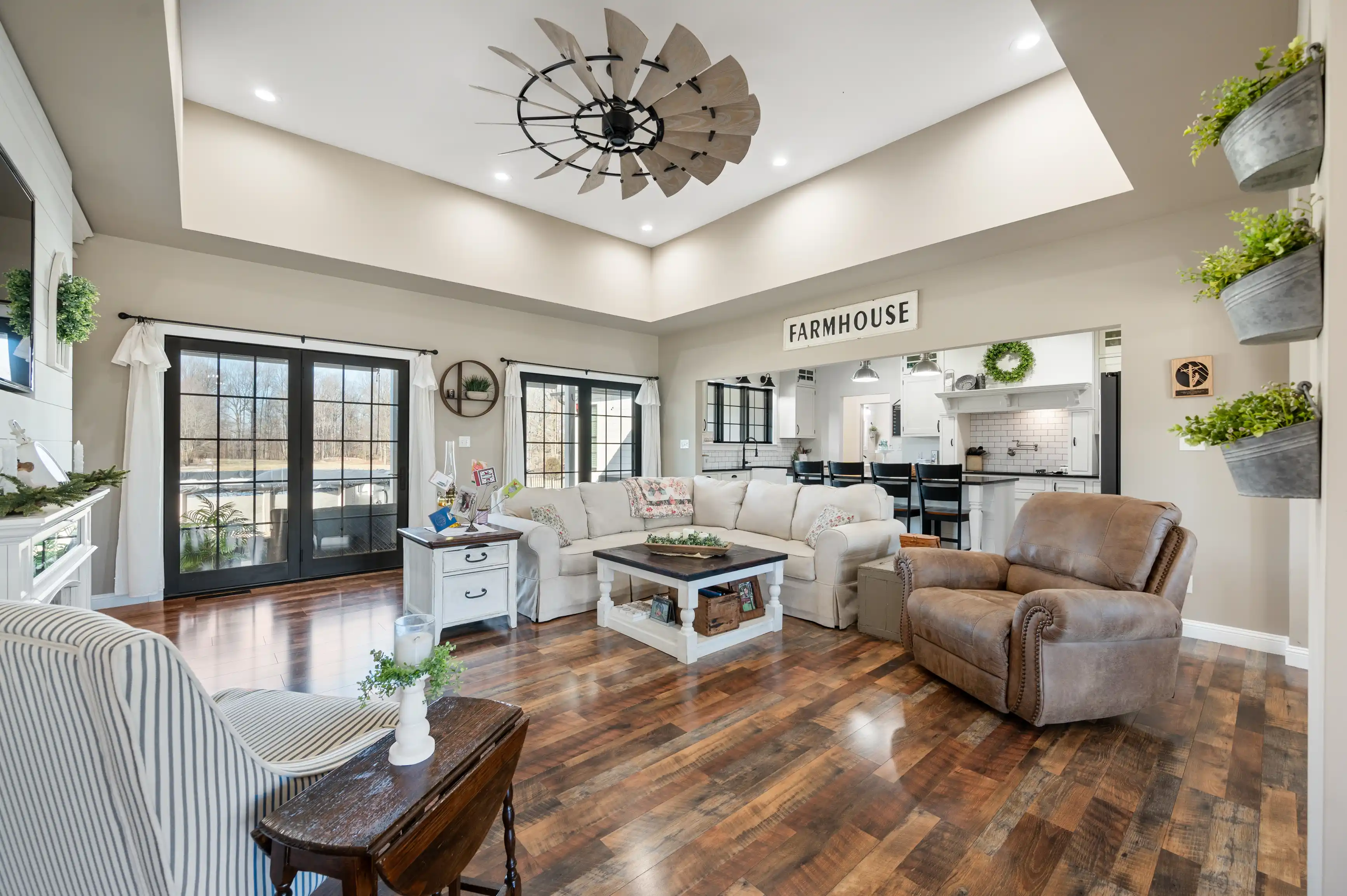 Bright and airy open-concept living room with farmhouse-style decor, vaulted ceiling and hardwood floors, leading into a kitchen with black accents.
