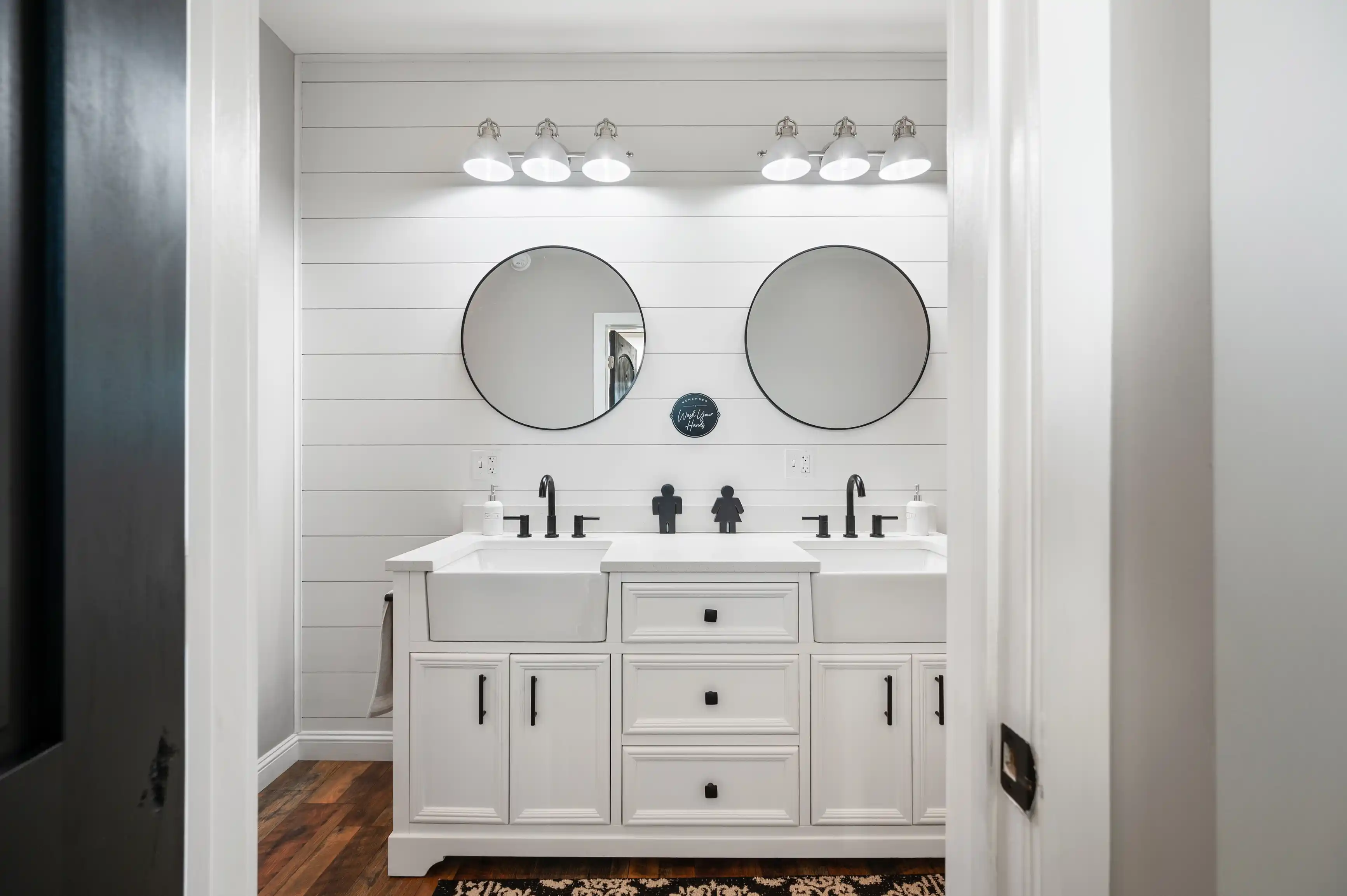 Modern bathroom interior with double sink vanity, black fixtures, two round mirrors, and shiplap wall.