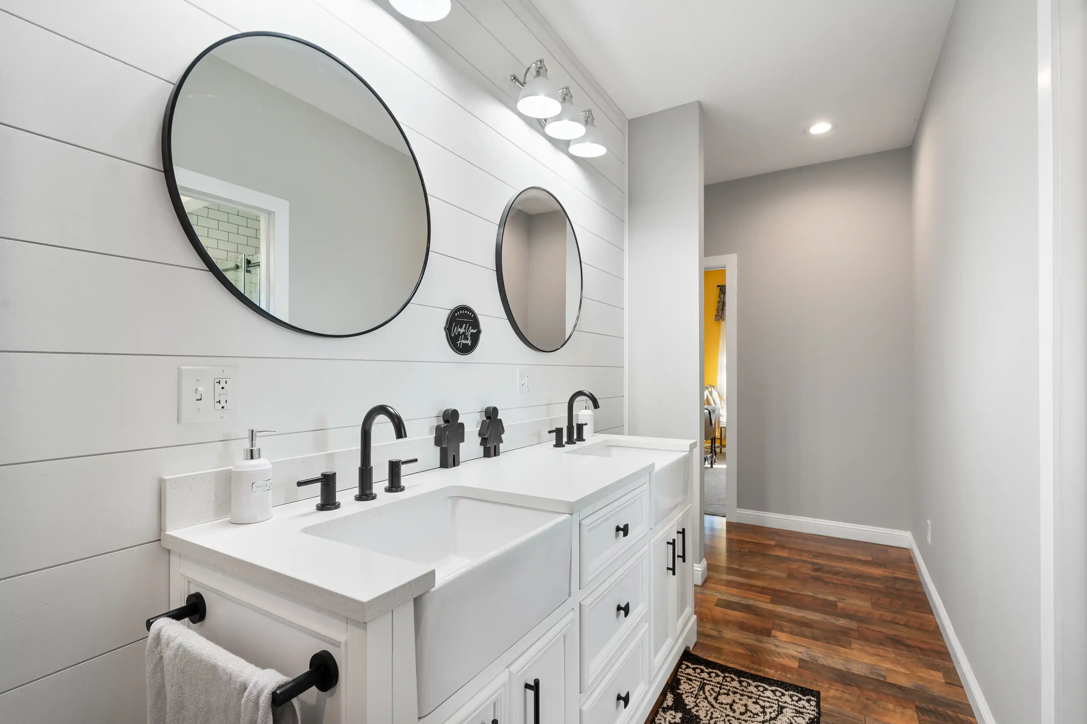 Modern bathroom interior with double sink vanity, large round mirrors, shiplap walls, and hardwood floors.