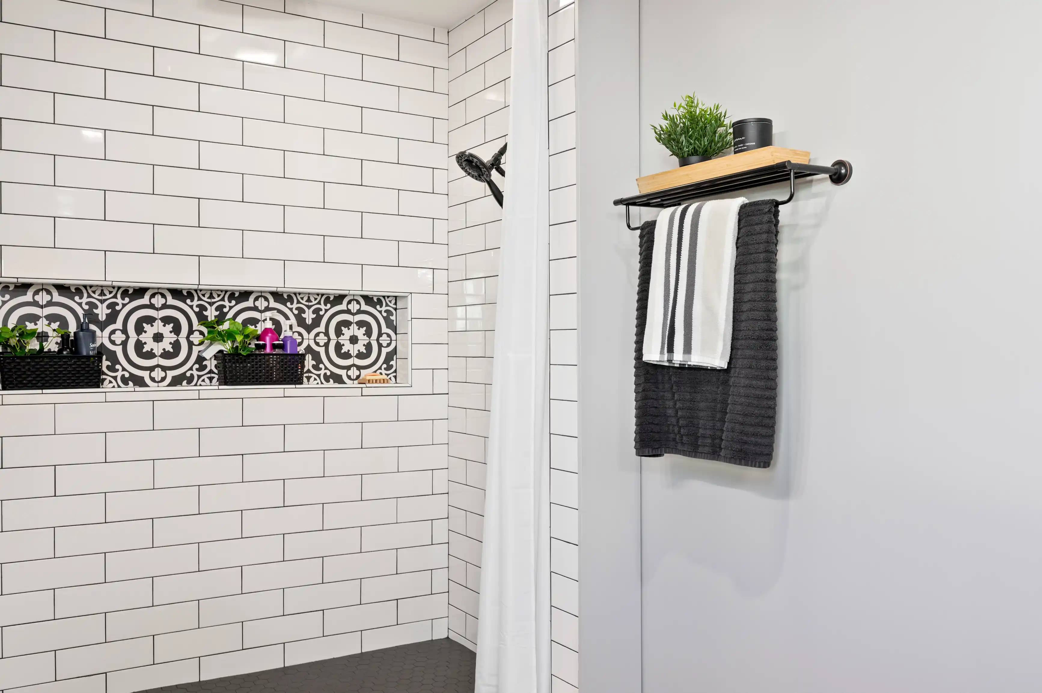 Modern bathroom interior with white subway tiles, decorative patterned accent tiles, shower head, and towel rack with black and white towels.