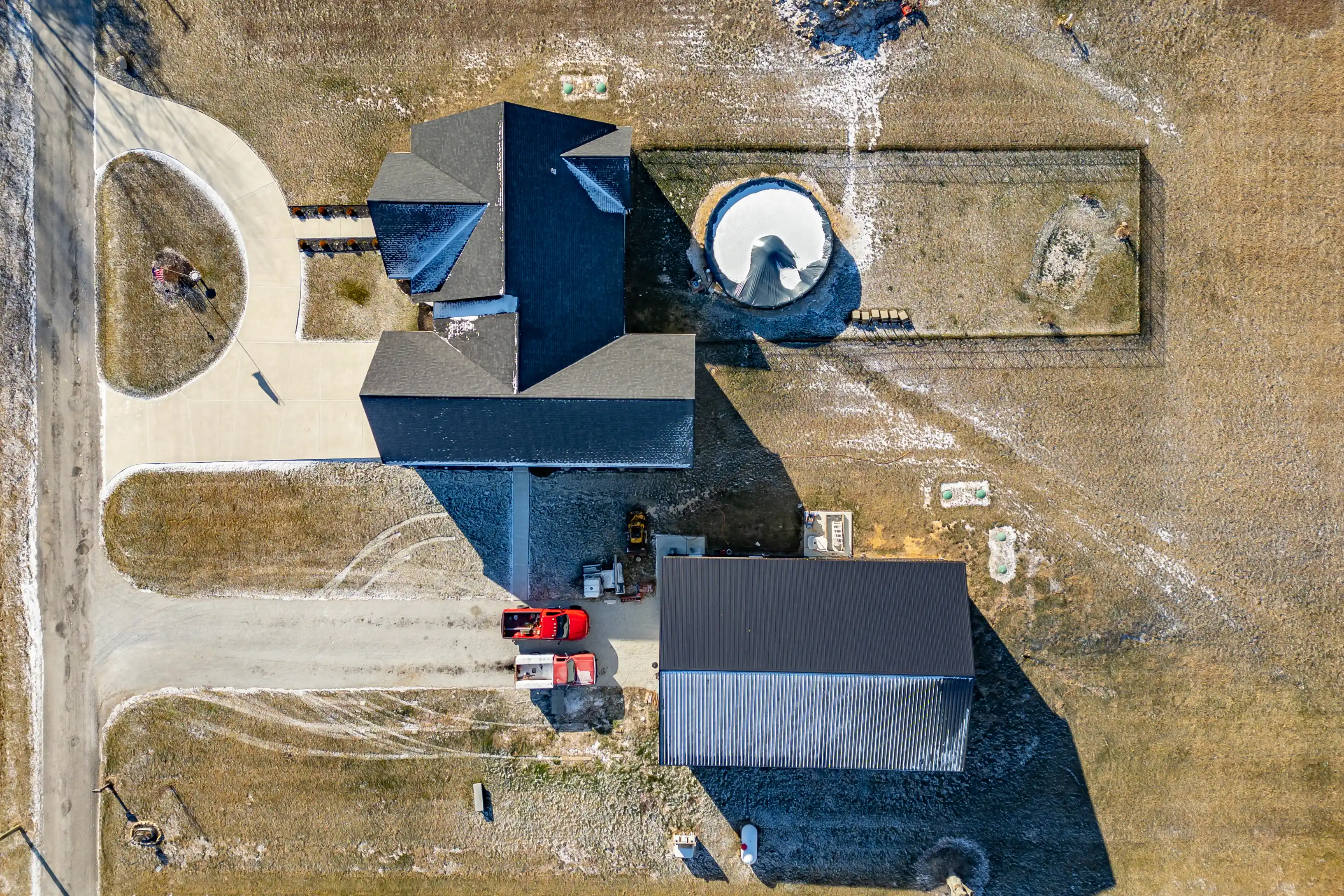 Aerial view of a rural property with a house, separate garage, curved driveway, and a silo.