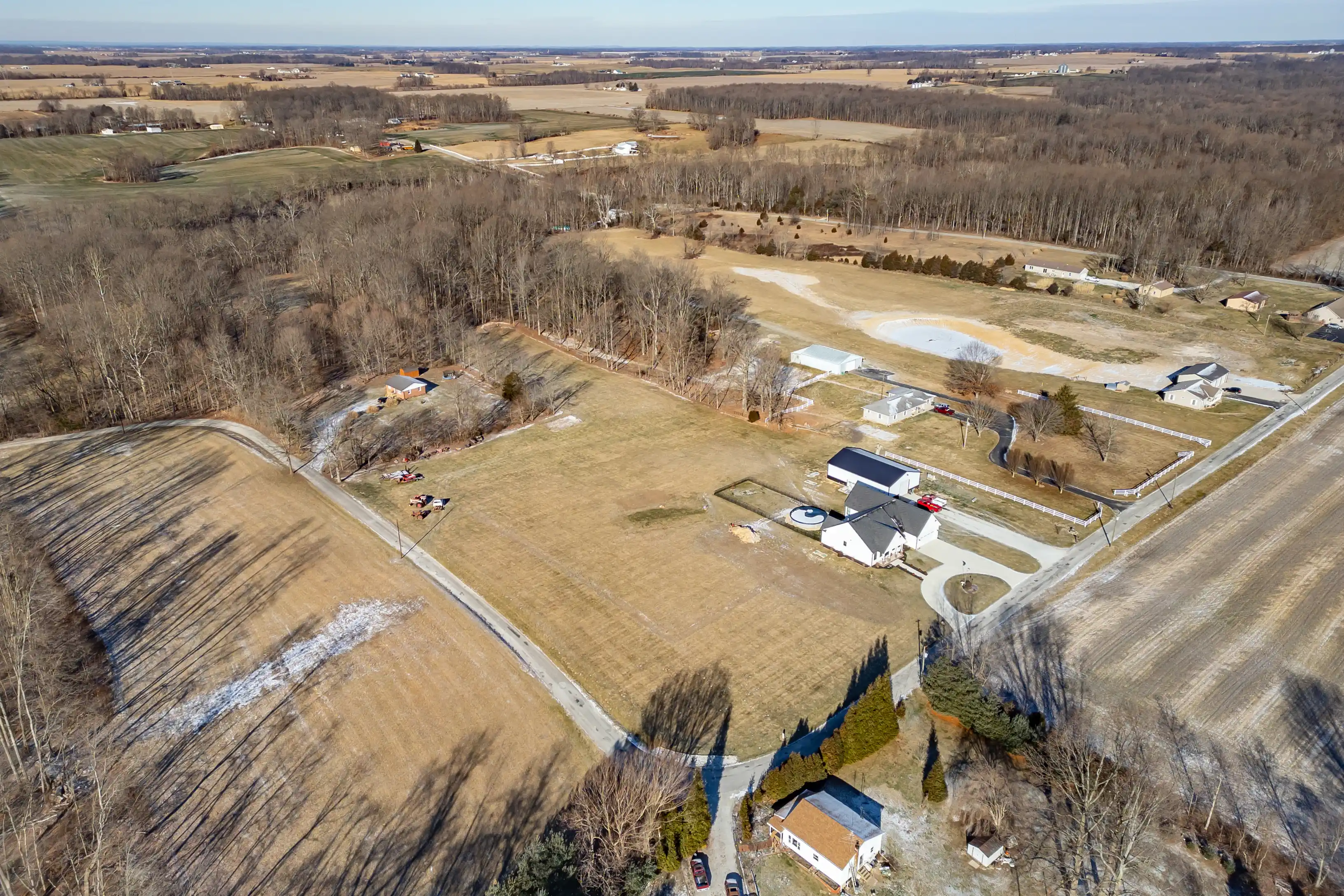 Aerial view of a rural landscape showing farmlands, houses, bare trees, and roads on a sunny day.