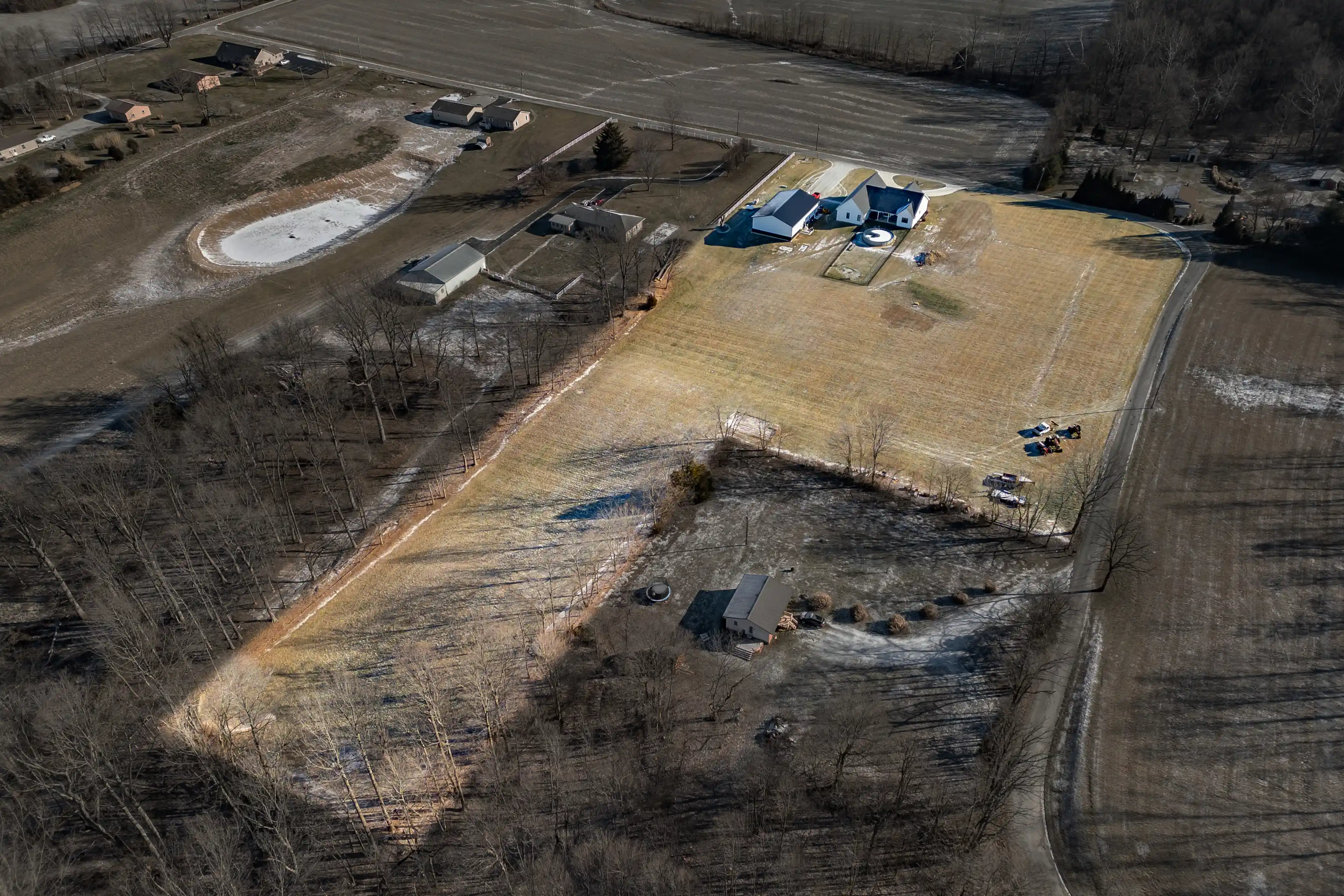 Aerial view of a rural landscape with a house, outbuildings, and bare trees during winter.