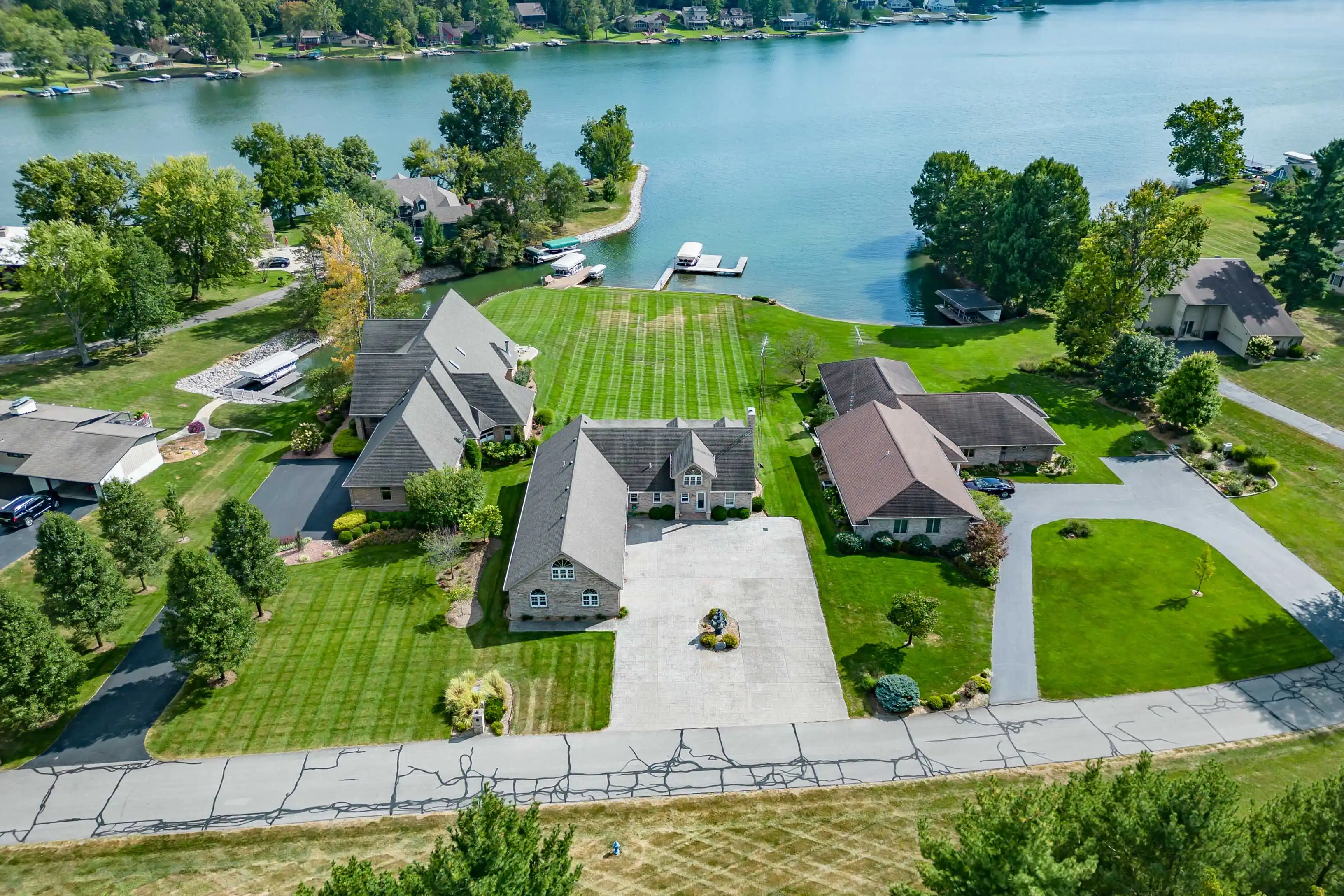 Aerial view of a residential area with manicured lawns, several houses, and a lake with docks and boats.
