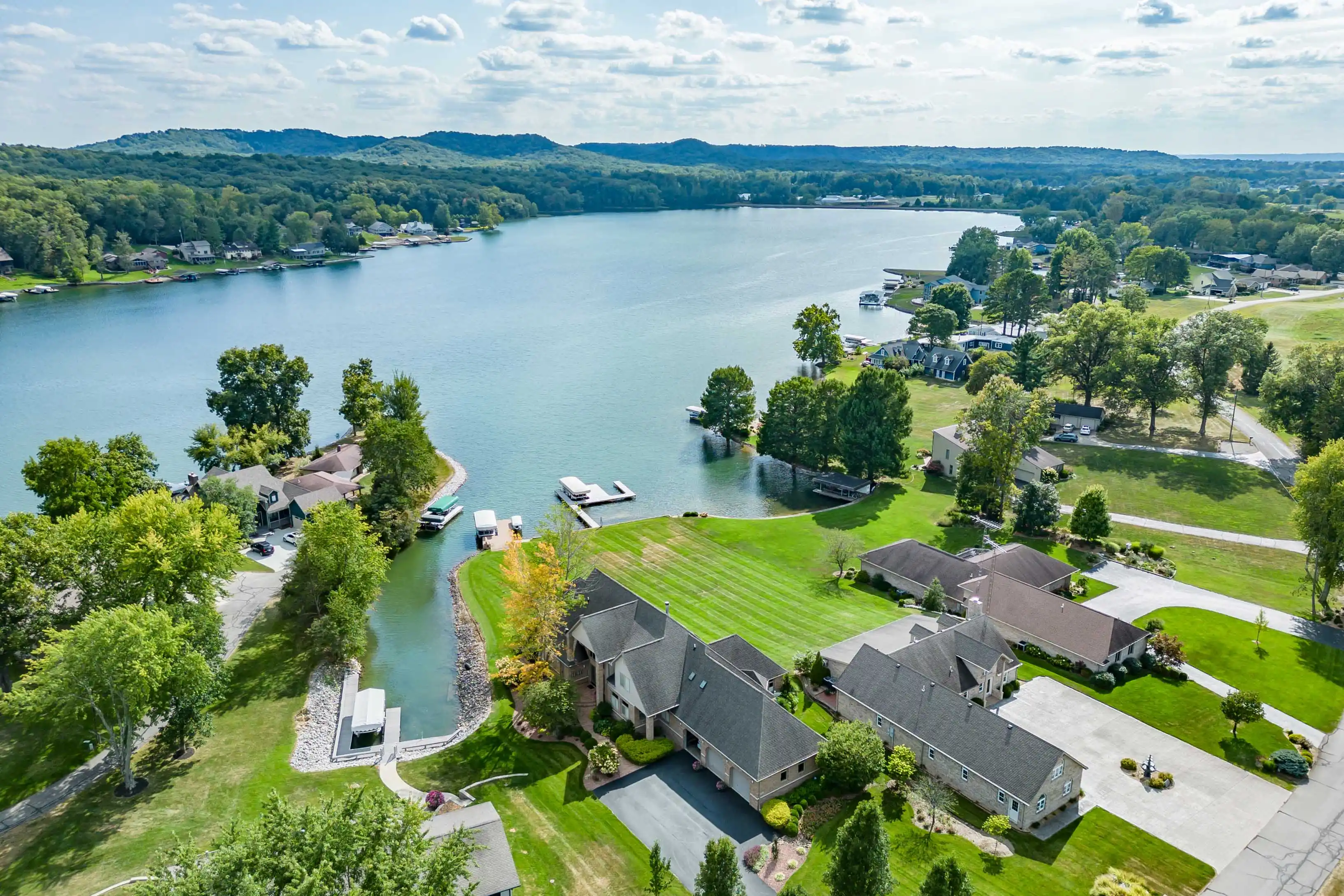 Aerial view of a residential area with houses, lush green lawns, and docks along the edge of a serene lake.