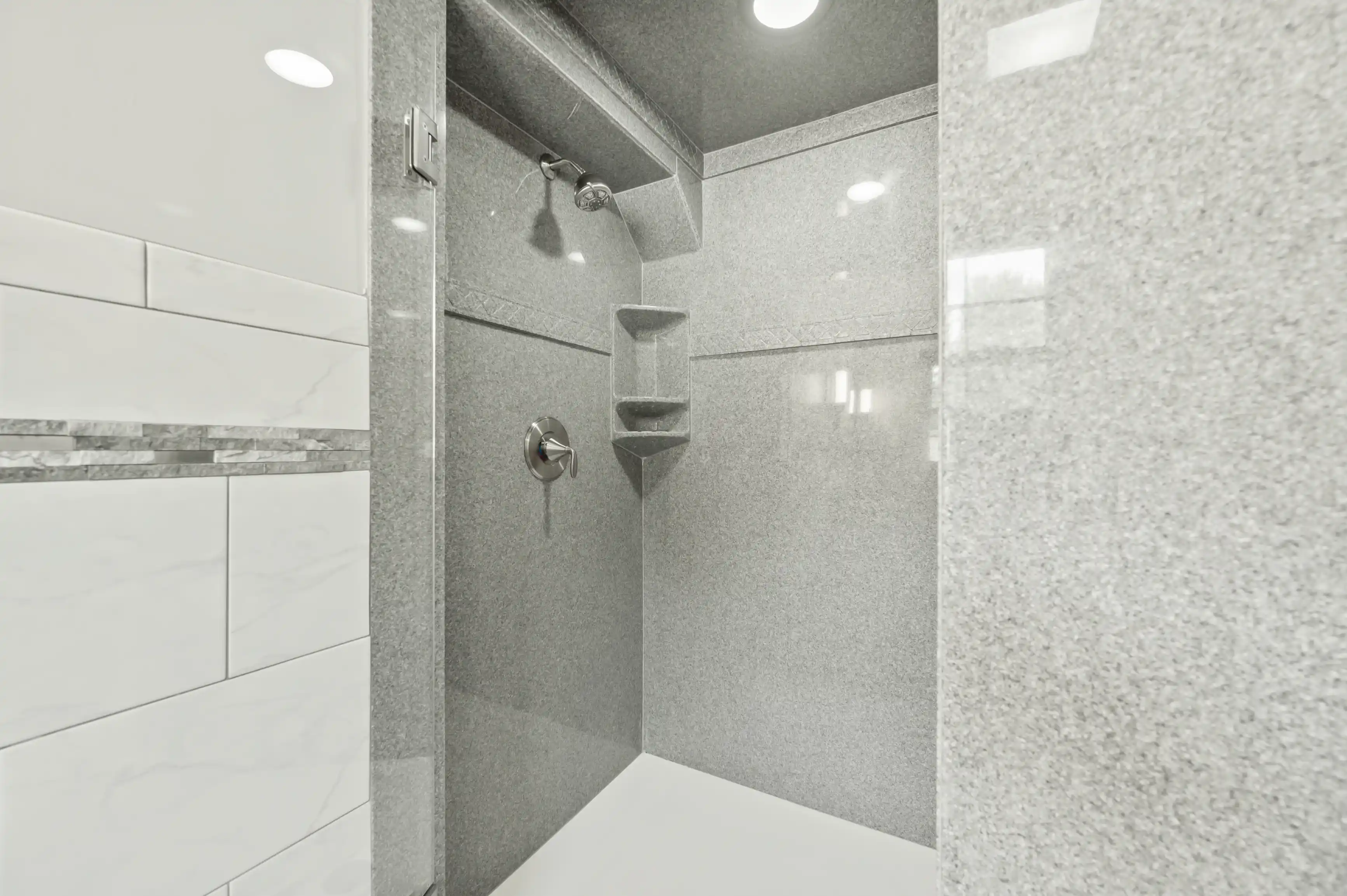 Modern shower interior with gray tiles, built-in shelf, and glass door.