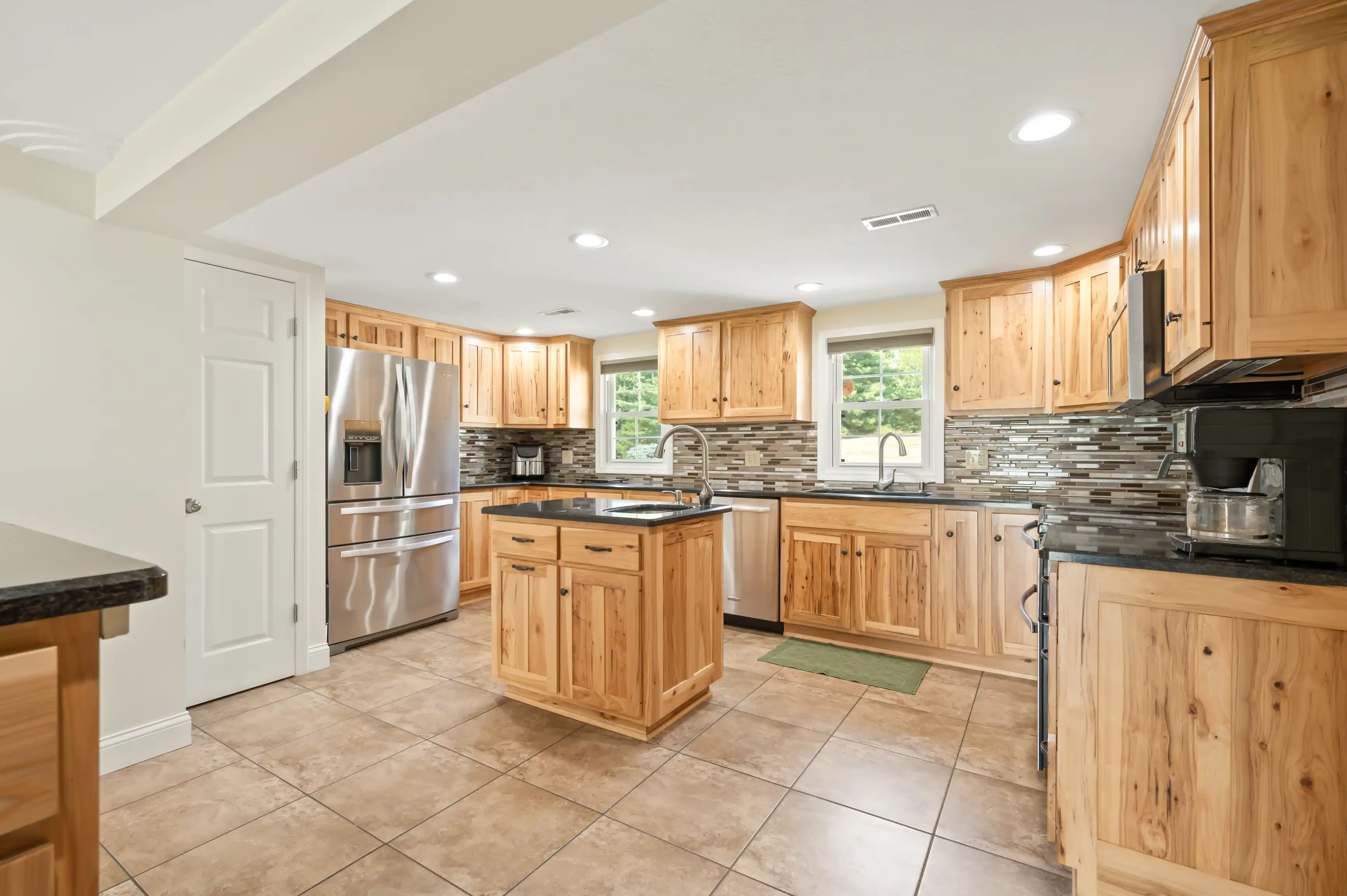 Spacious kitchen with natural wood cabinets, stainless steel appliances, and a stone tile backsplash.