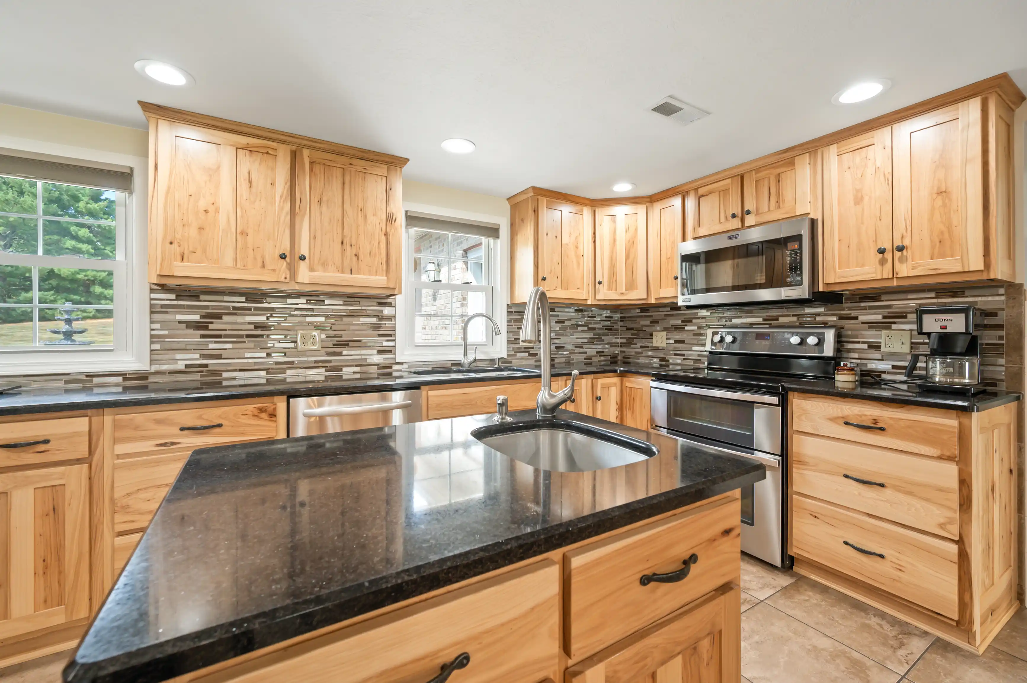 Bright, spacious kitchen with natural wood cabinets, stainless steel appliances, and a tiled backsplash.