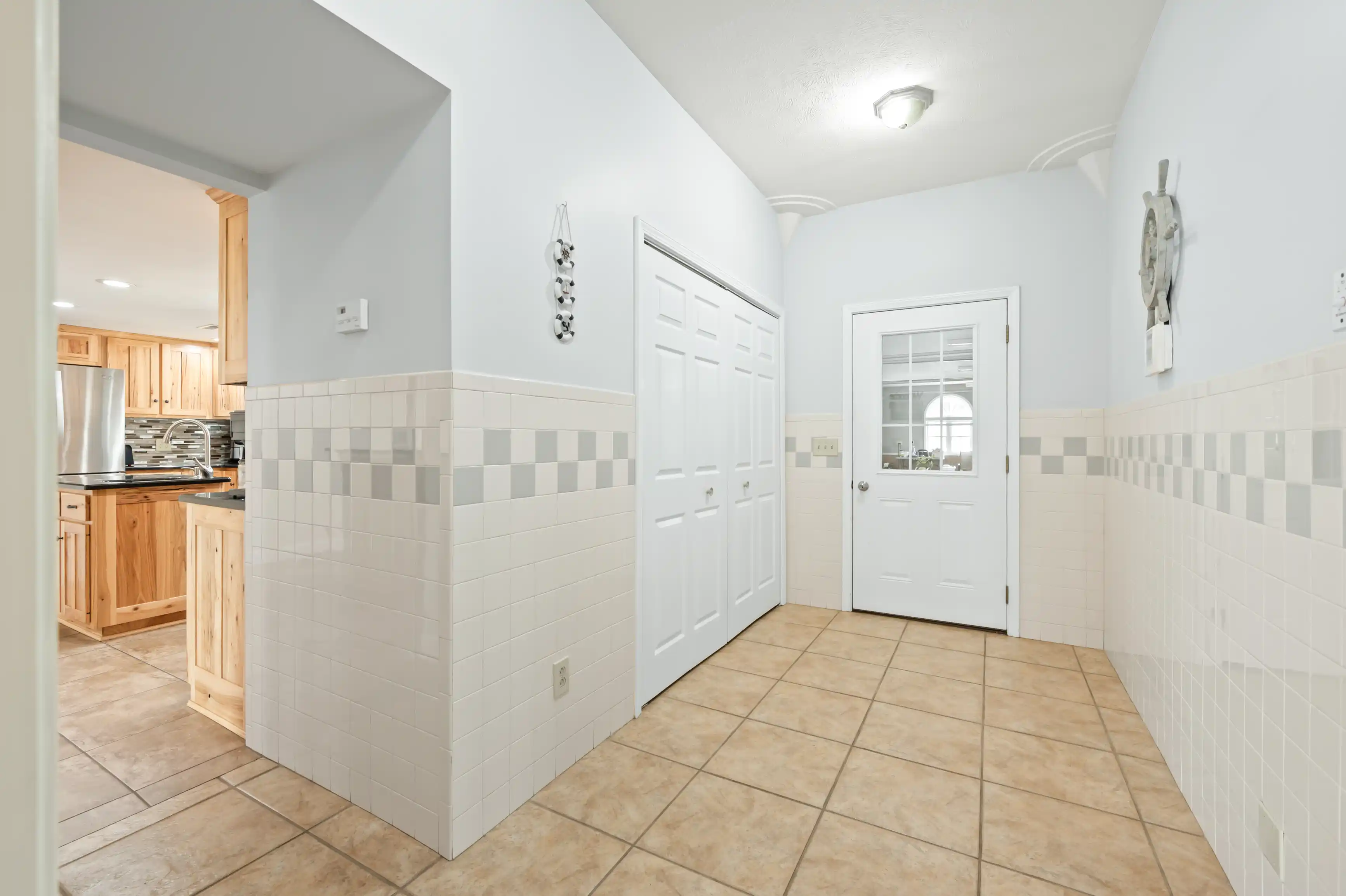 Bright and clean tiled entryway leading to a kitchen with wooden cabinets and modern appliances.