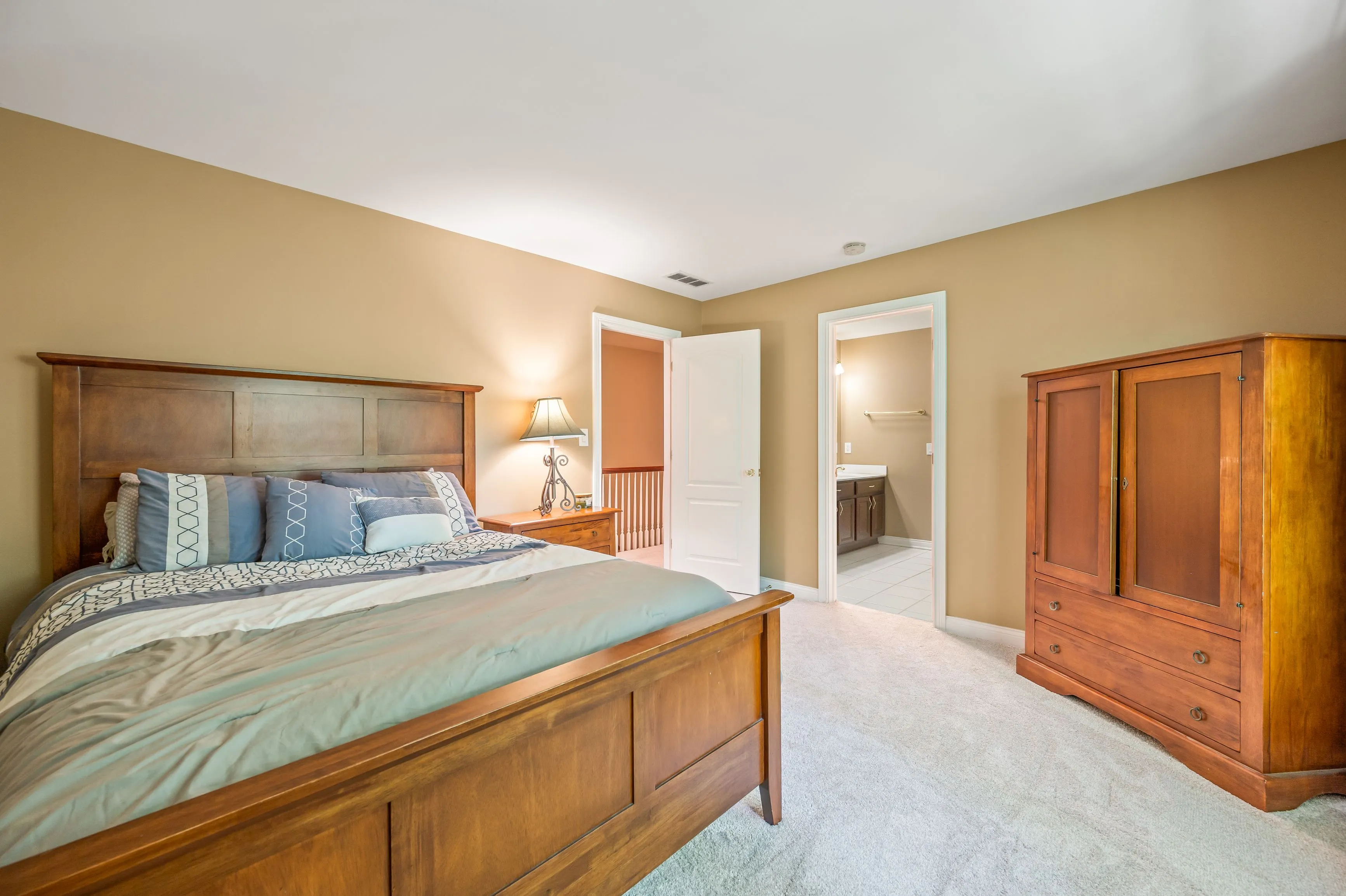 Spacious bedroom with large bed, wooden furniture, and open doors leading to another room.
