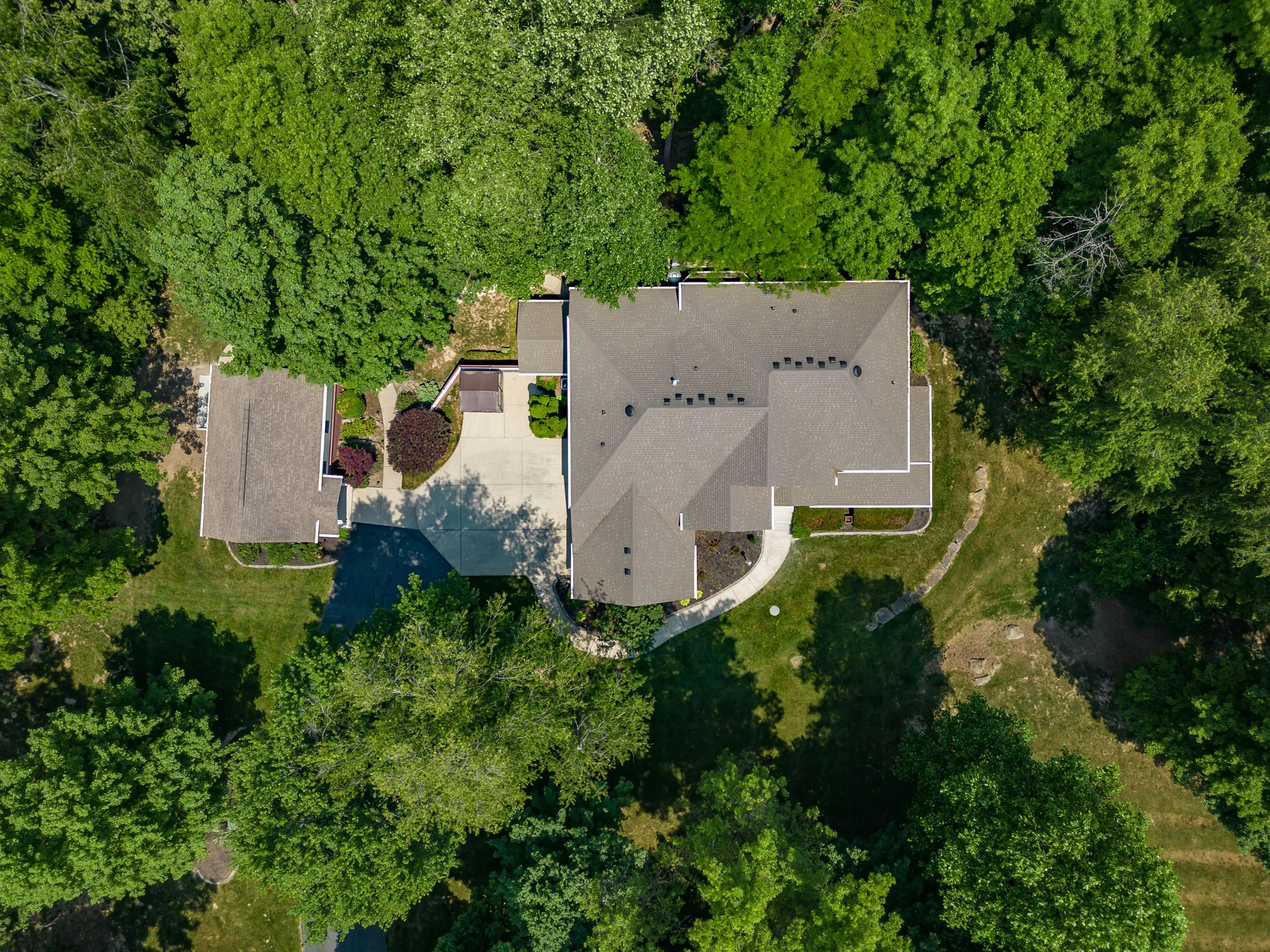 Aerial view of a large house with multiple roofs surrounded by dense green trees.