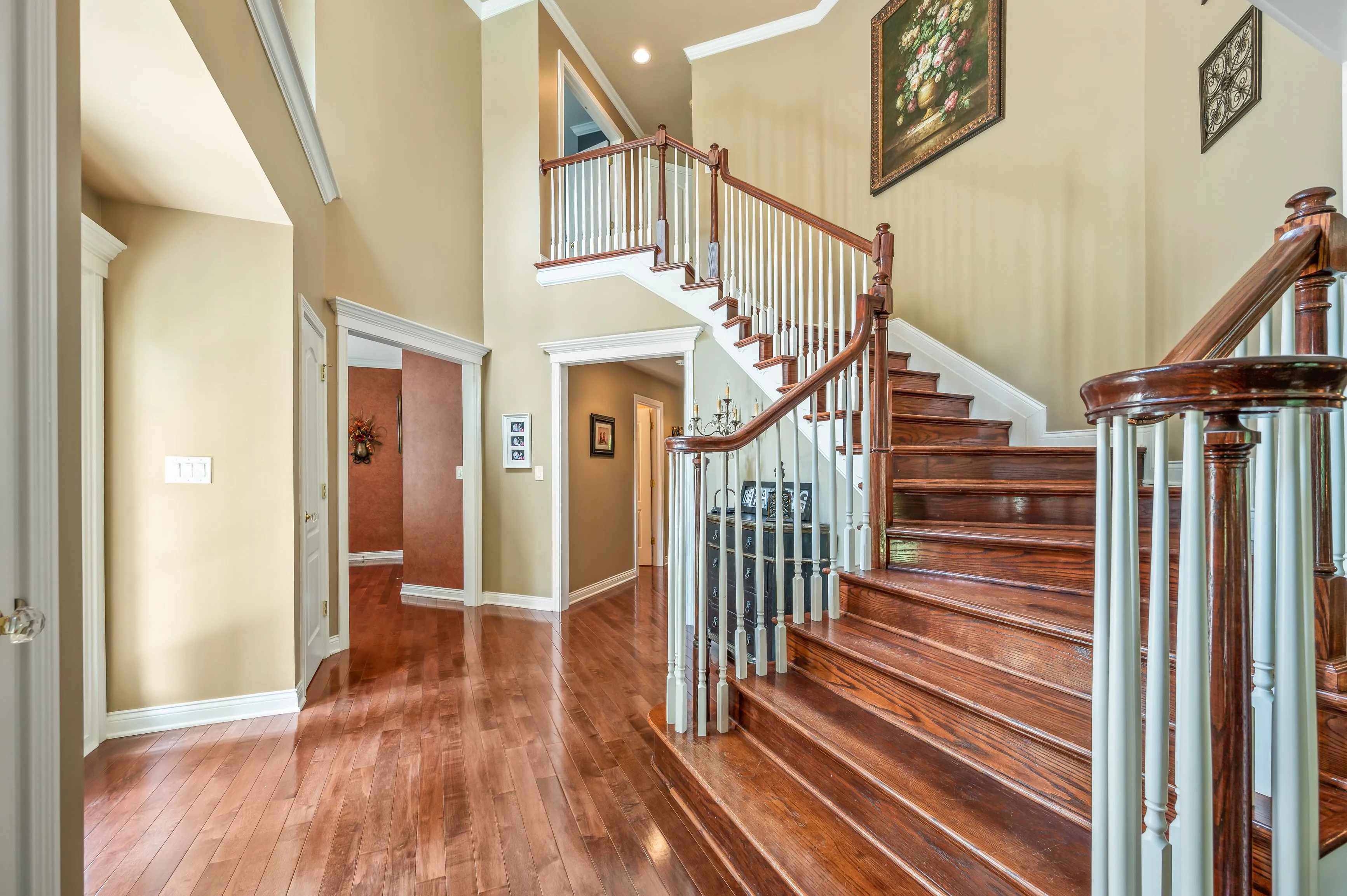 Elegant home interior with wooden staircase and floors, beige walls, and multiple doorways.