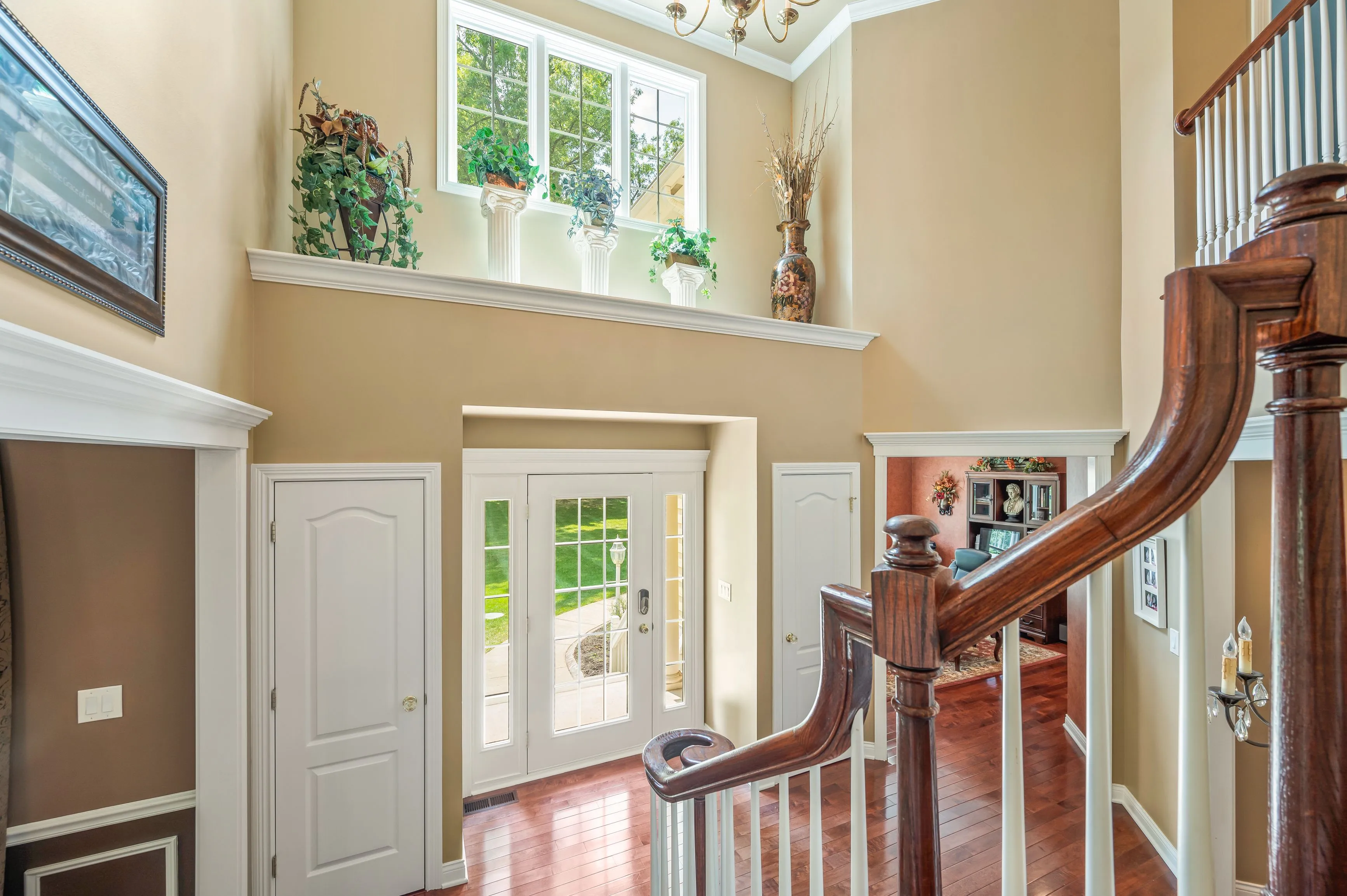 Elegant interior of a home foyer with a wooden staircase, high ceilings, and natural light from windows.
