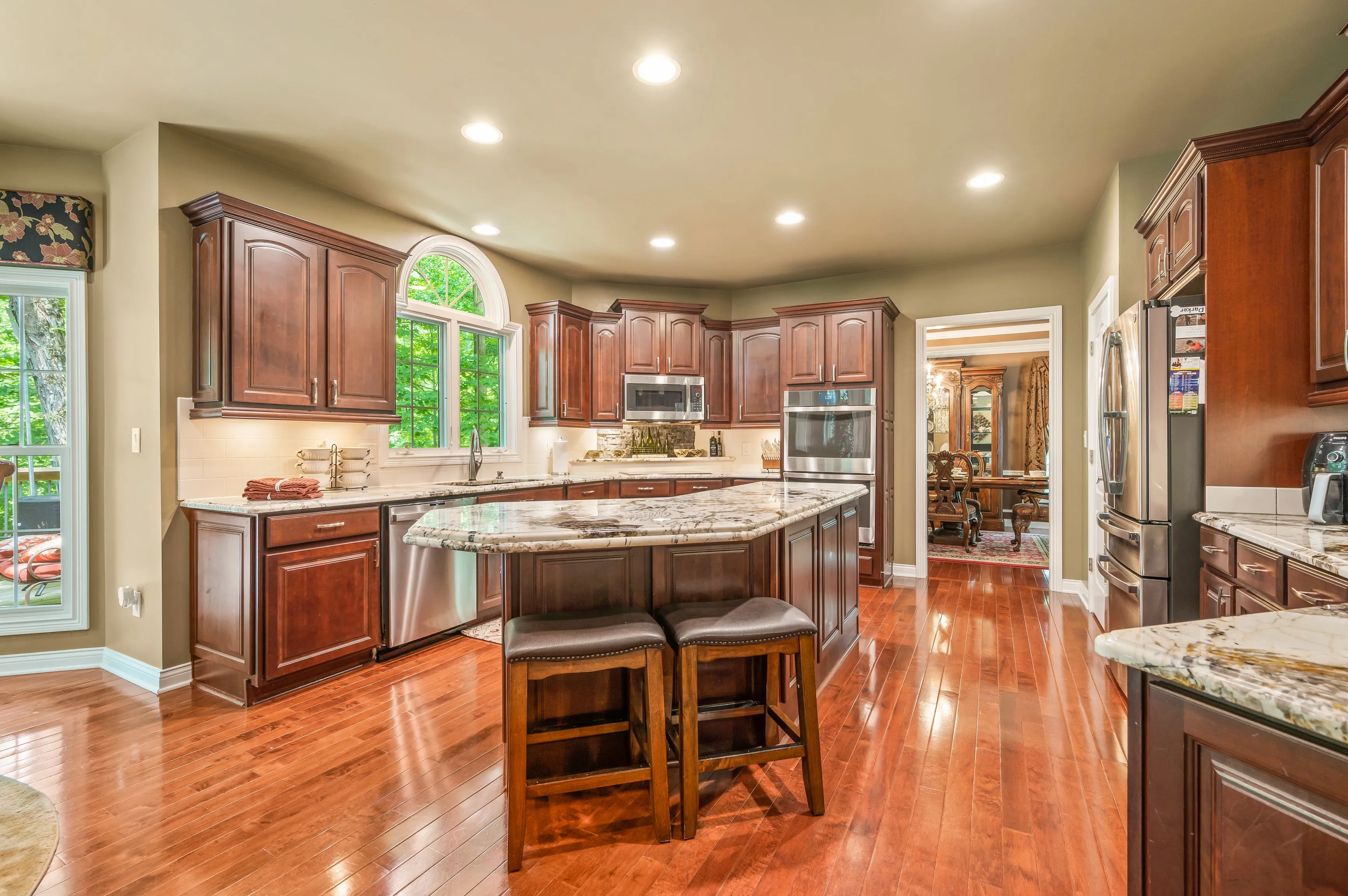 Spacious kitchen interior with polished hardwood floors, rich wooden cabinetry, and a central island with granite countertop.