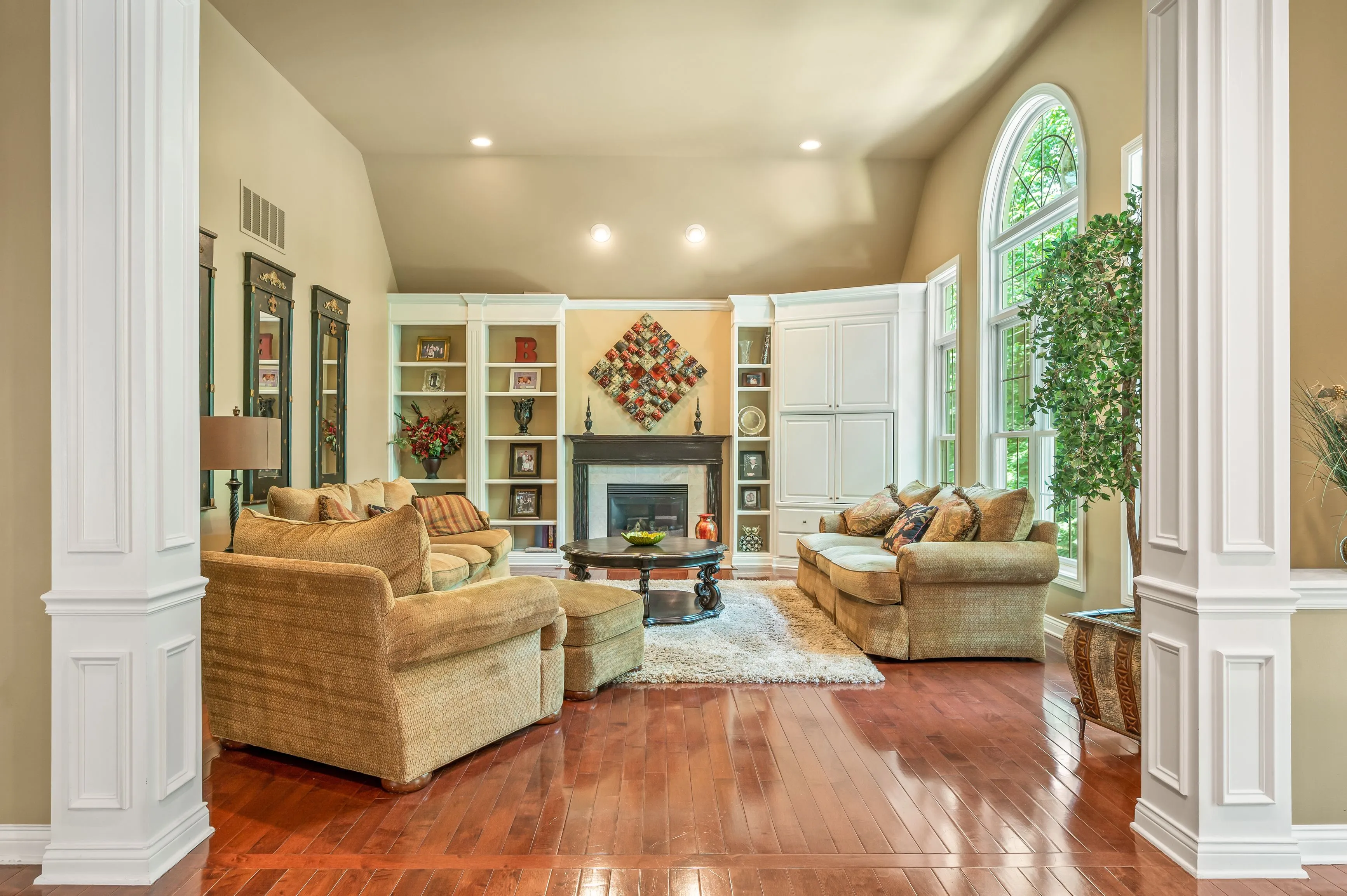 Elegant living room with polished hardwood floors, white columns, fireplace, large windows, and comfortable furniture.