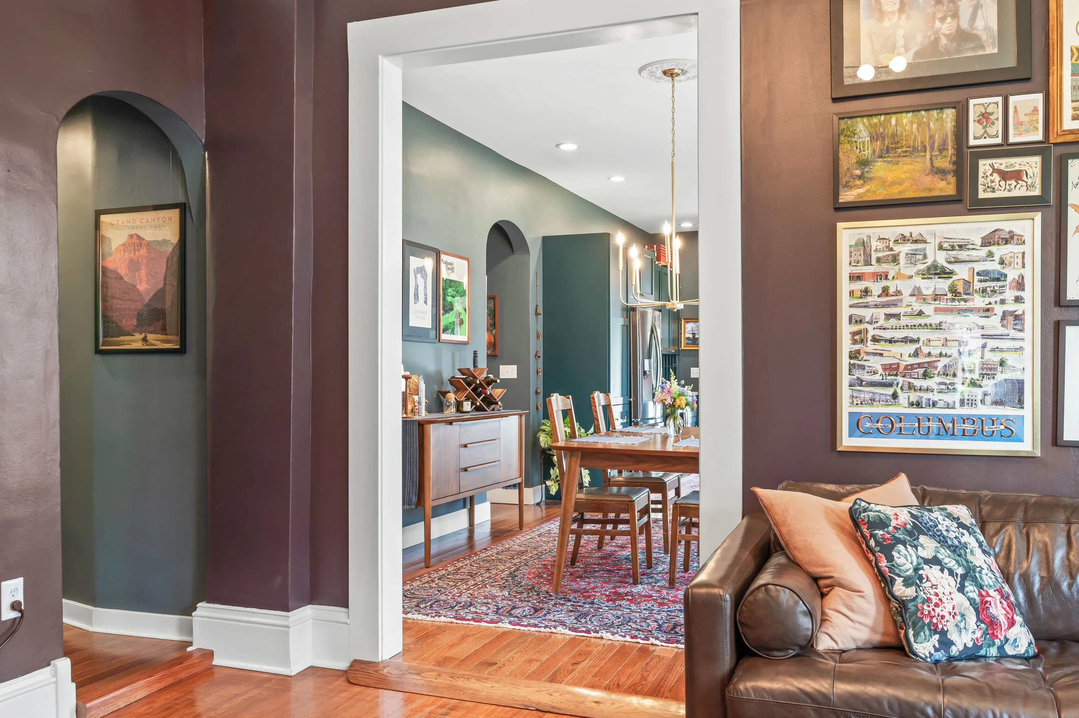 Elegant interior view of a home with hardwood floors, featuring a hallway leading to a dining area with framed pictures on the wall and decorative elements.