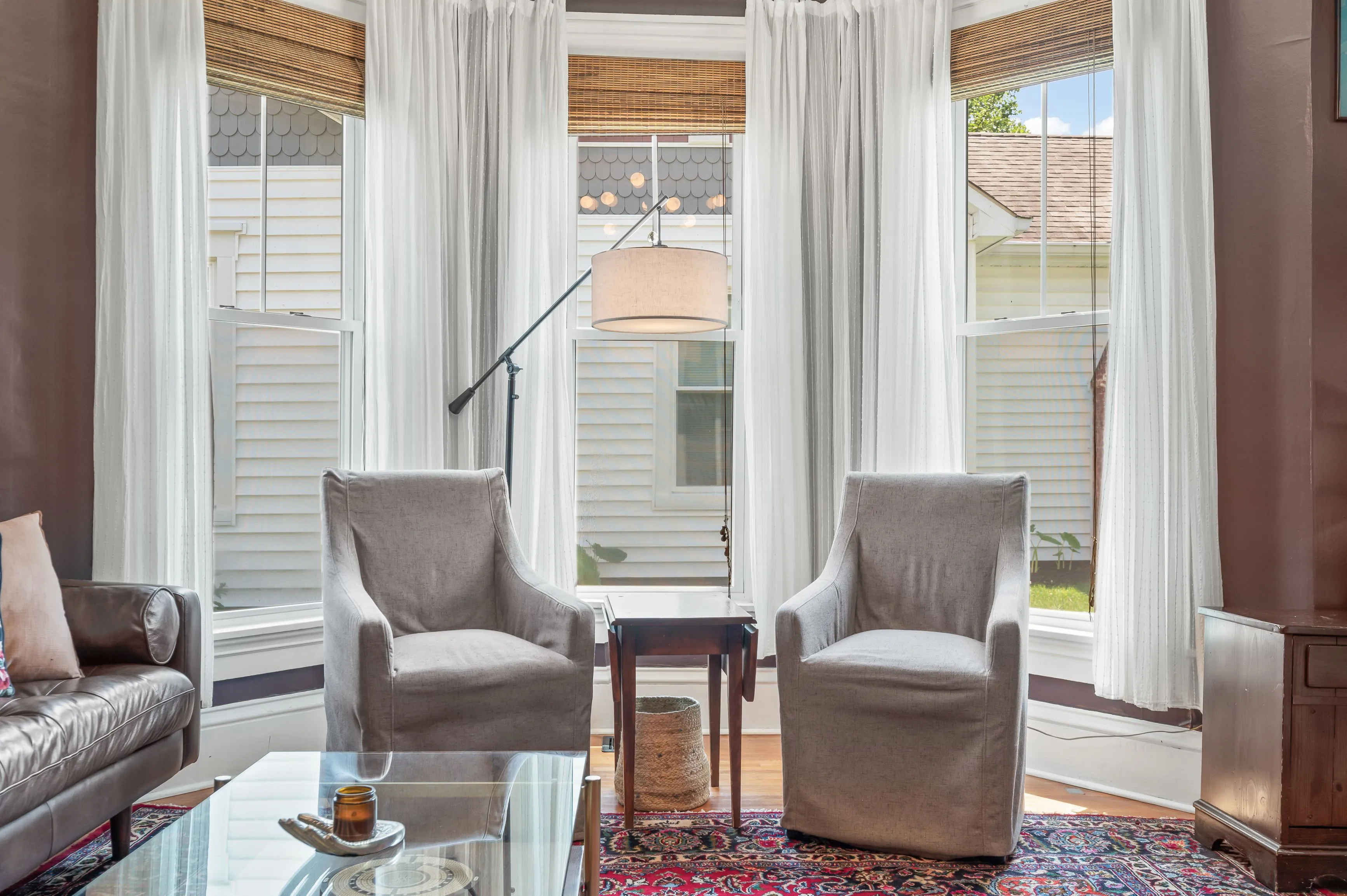 Bright living room interior with two armchairs, a sofa, sheer curtains, and a view of a balcony.