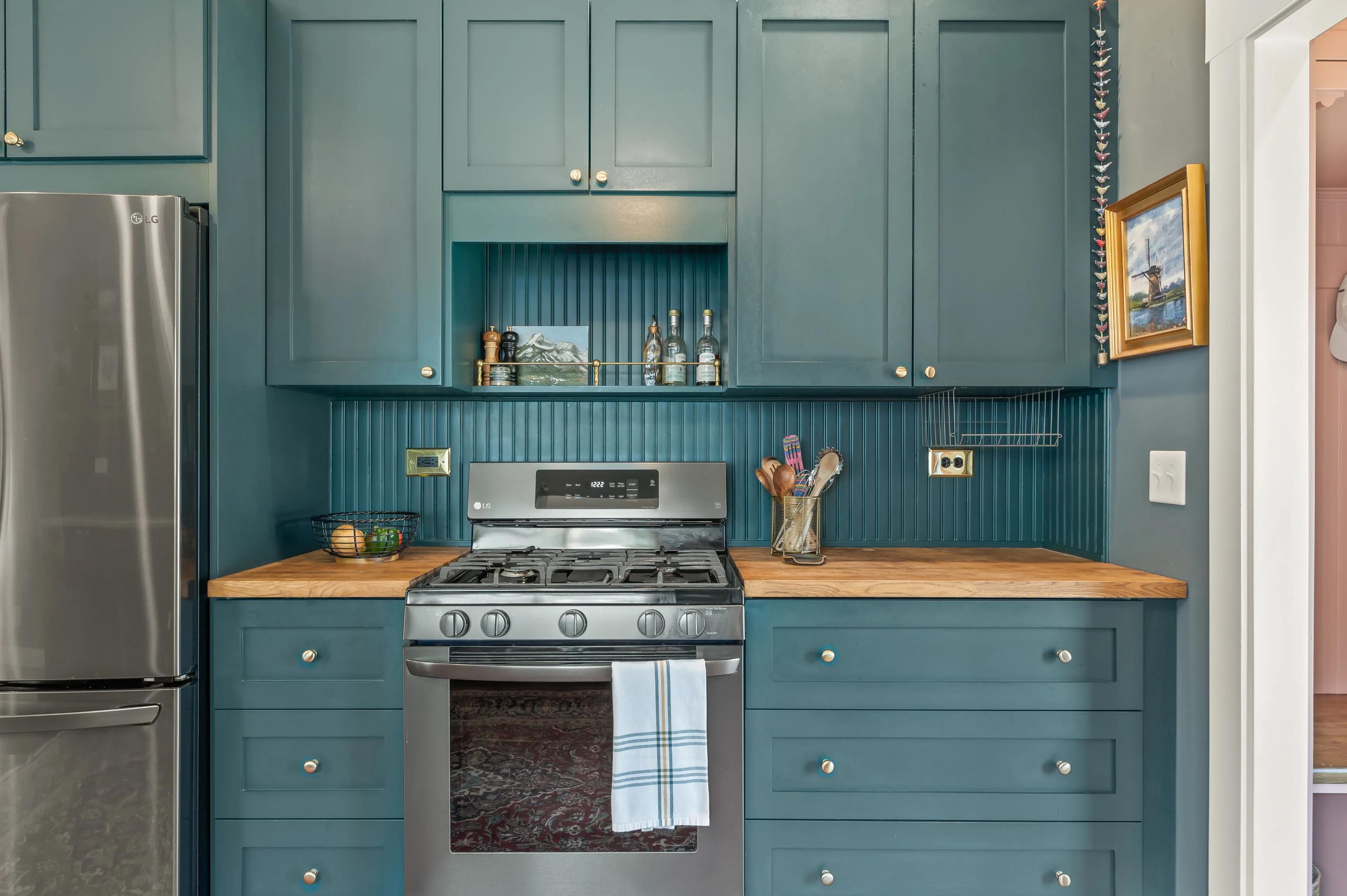 Modern kitchen with teal cabinetry, stainless steel appliances, and wooden countertops.