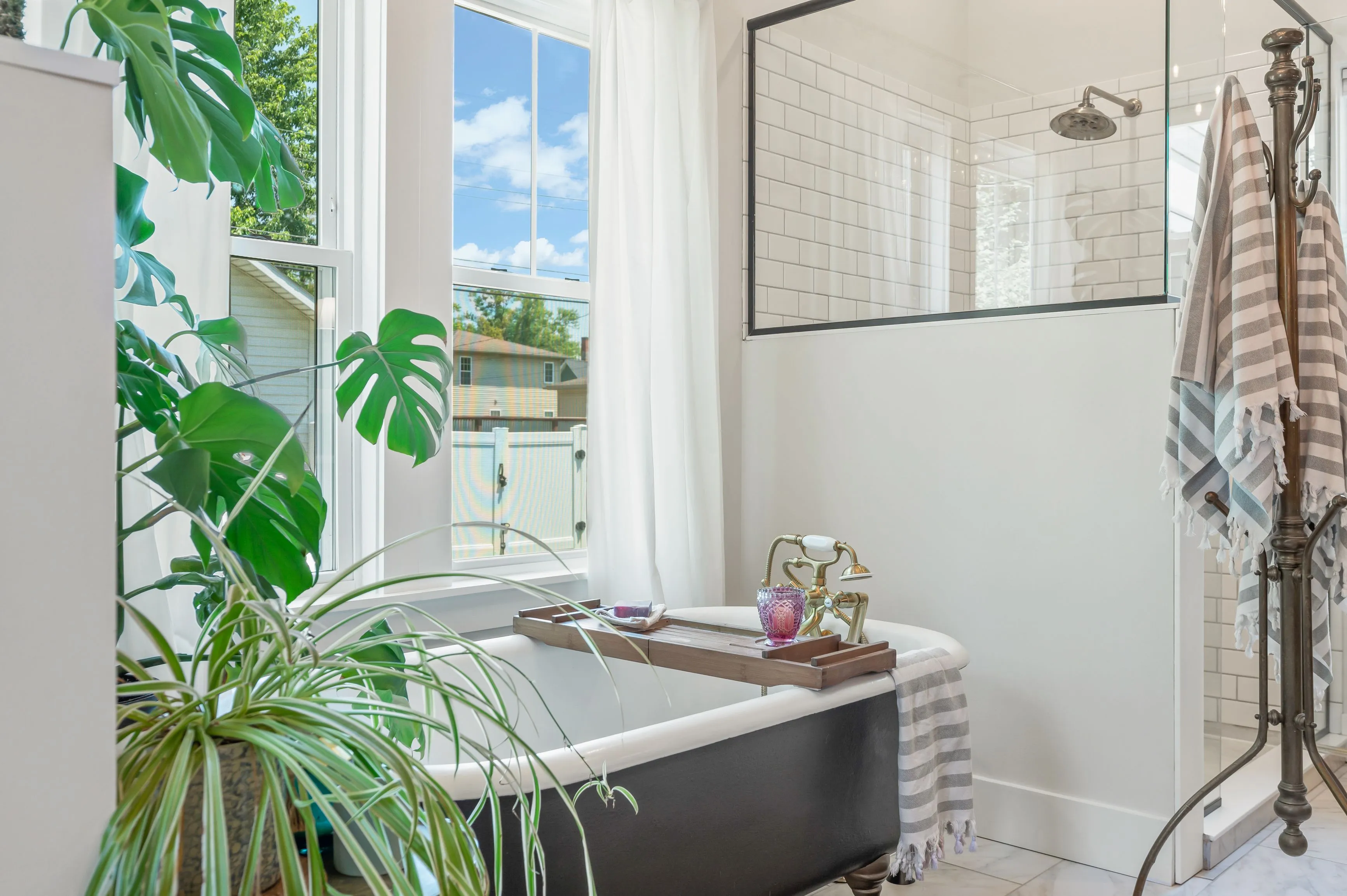 Bright bathroom interior with a freestanding tub, potted plants, and natural light coming through a window.