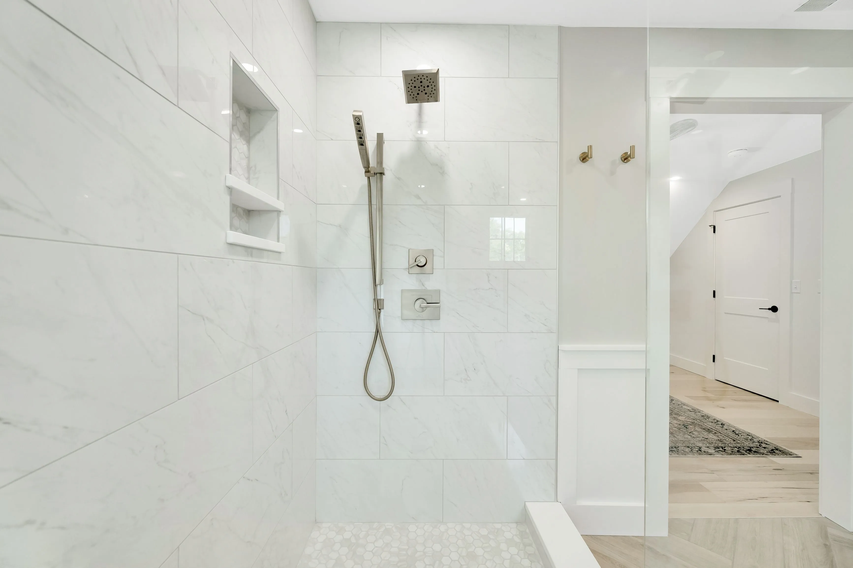 Modern bathroom interior with glass door walk-in shower, marble tiles, built-in wall shelf, and rainfall shower head.