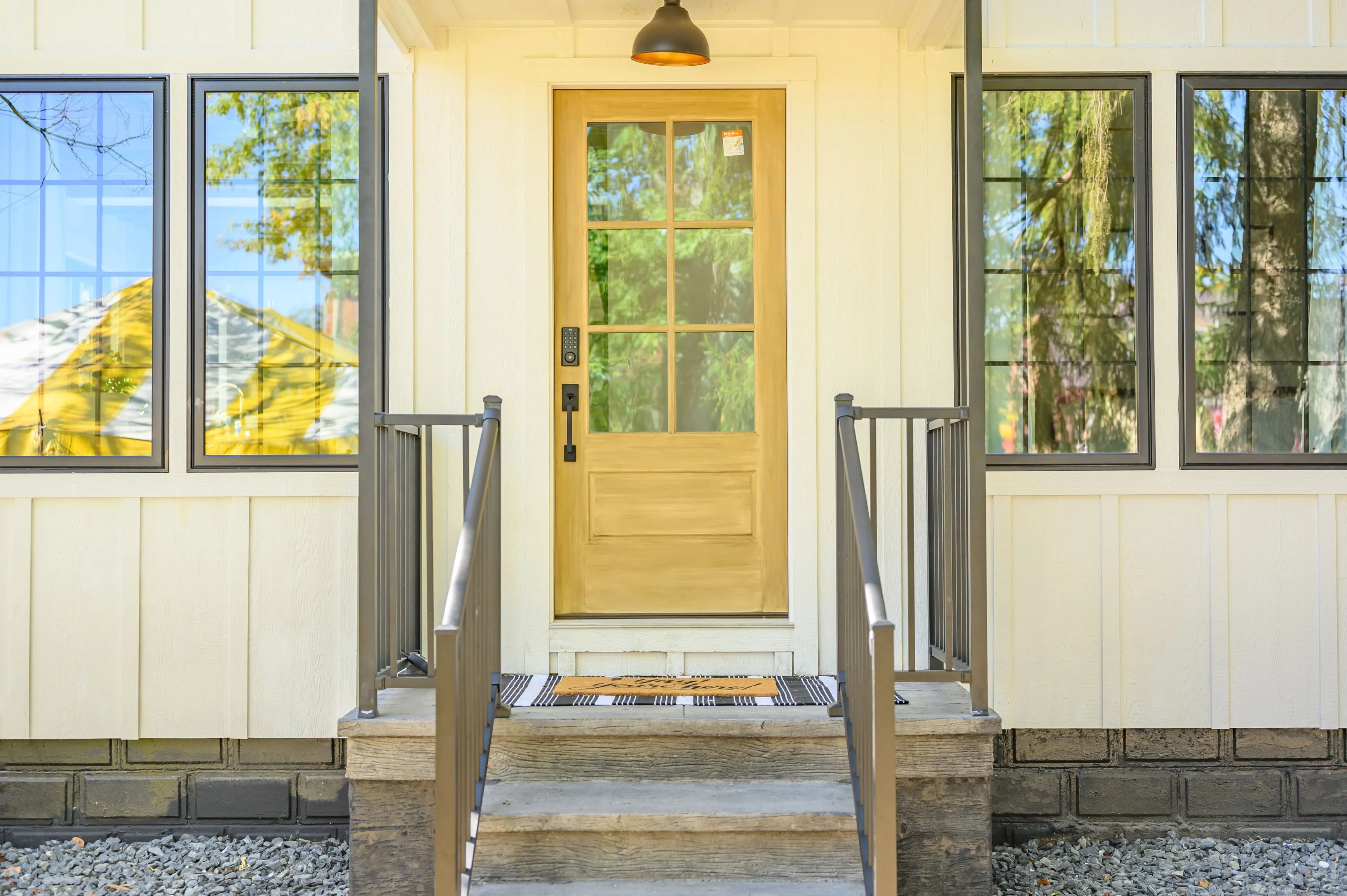 Front entrance of a modern house with a wooden door, glass side panels, and metal handrails on the steps.