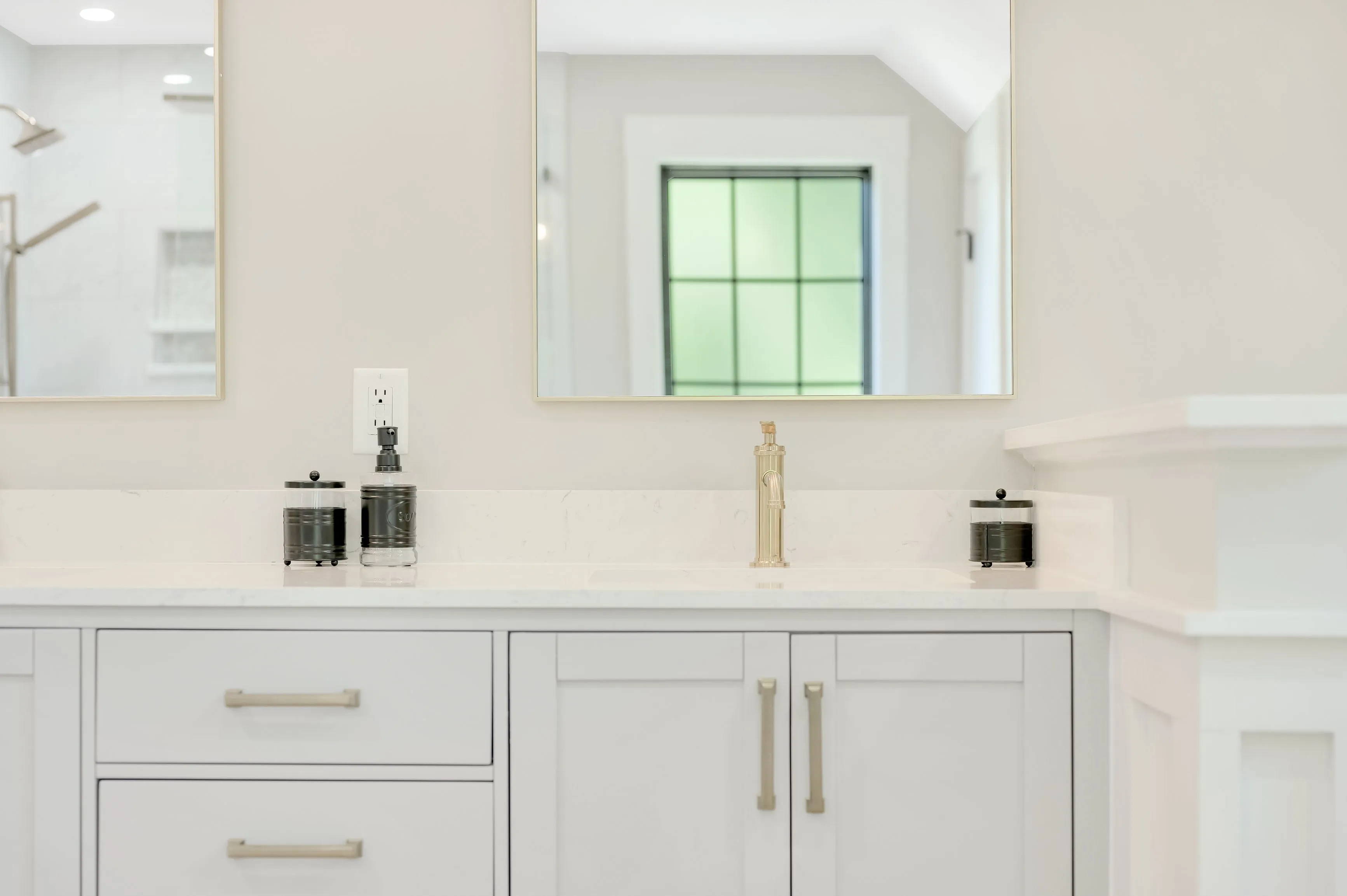 Elegant bathroom vanity with marble countertop, white cabinetry, and a large framed mirror reflecting a window.