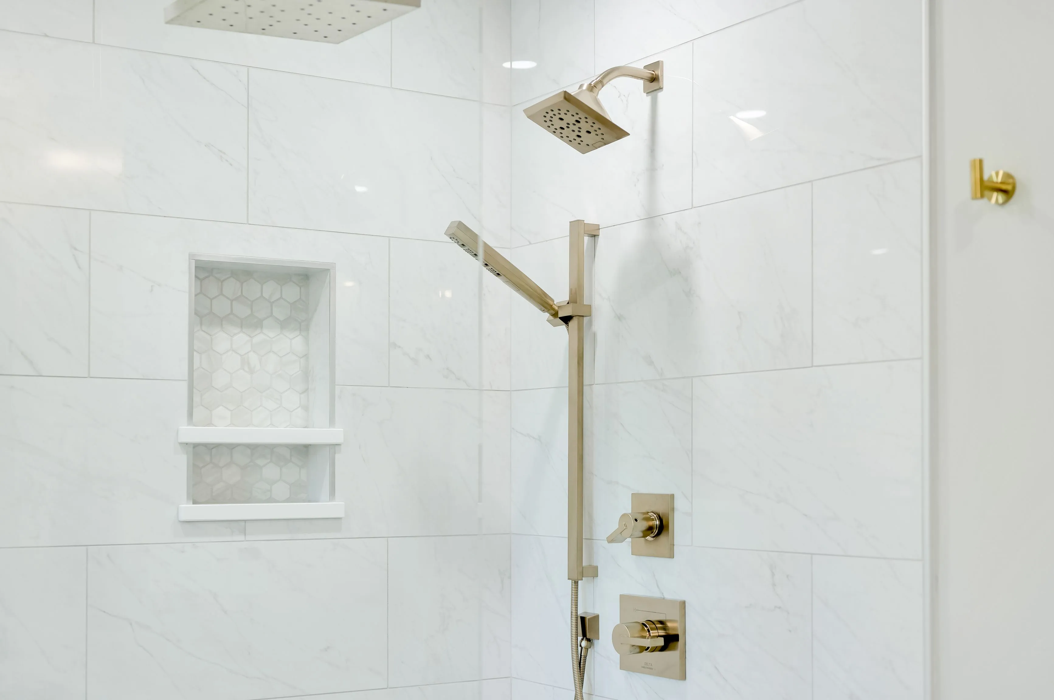 Modern shower with marble tiles, gold fixtures, built-in shelf, and dual shower heads.