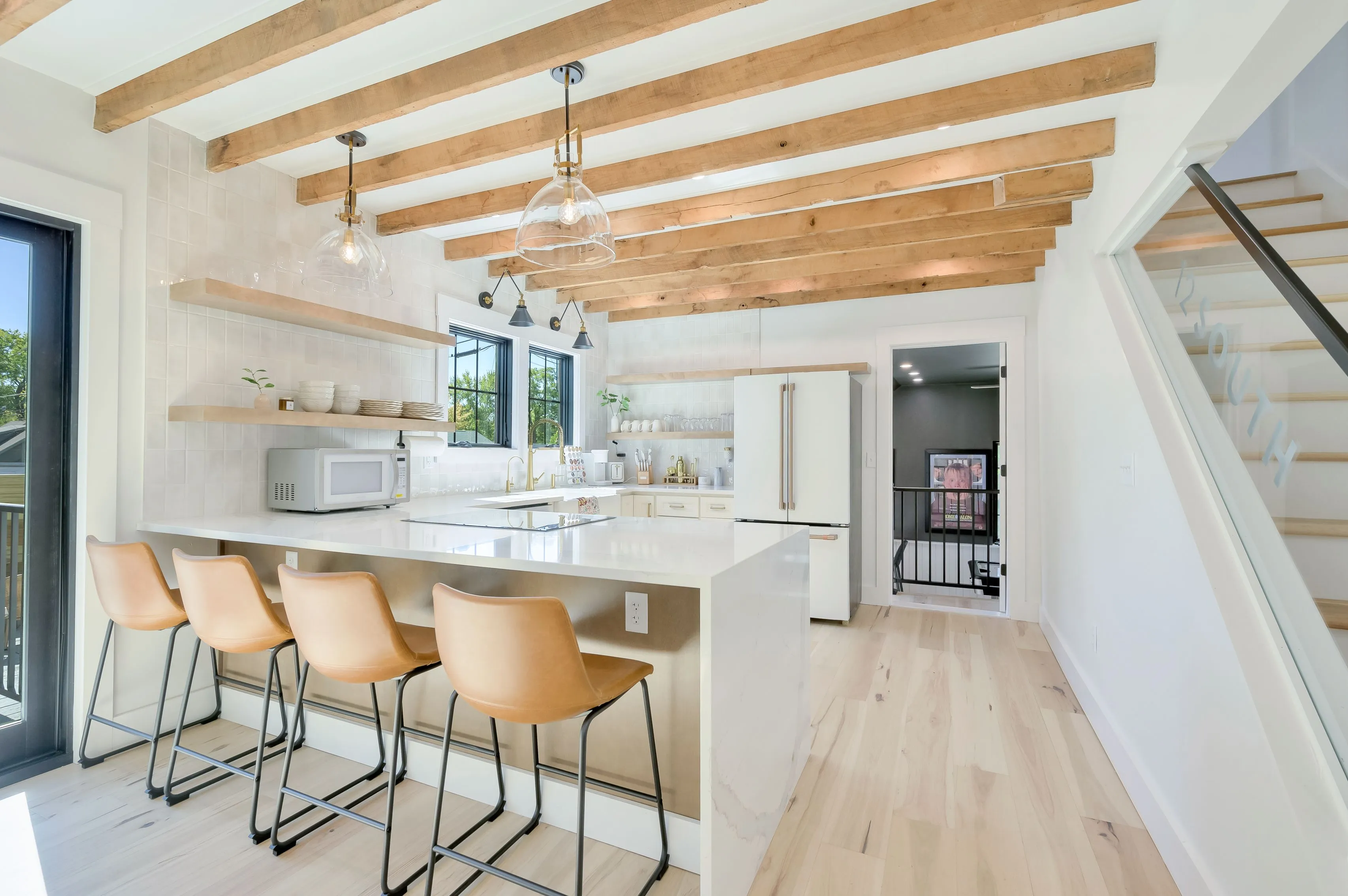 Bright modern kitchen with white countertops, wooden beams on the ceiling, and bar stools by the island.