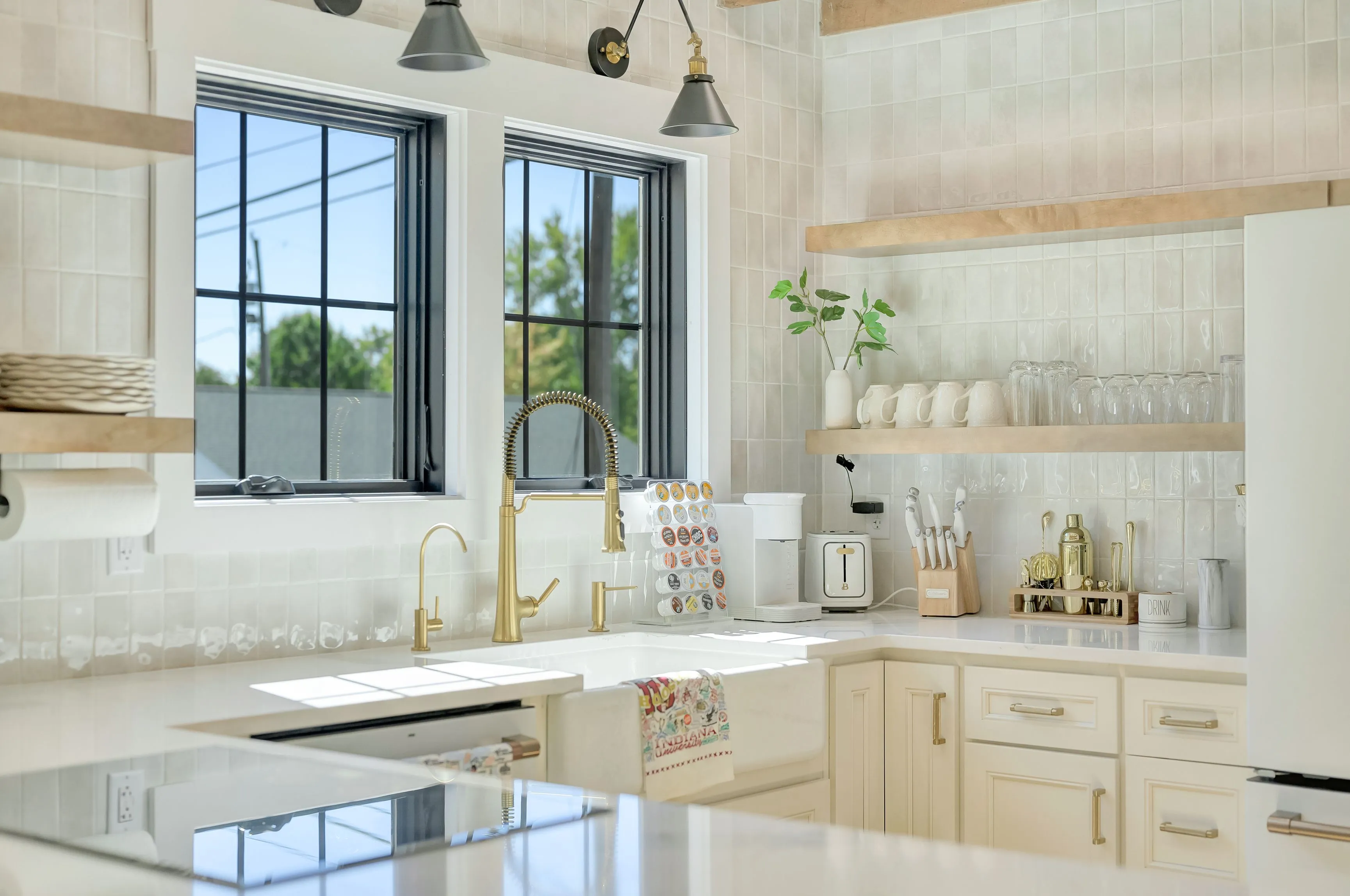 Bright modern kitchen interior with white countertops, brass fixtures, and floating wooden shelves.
