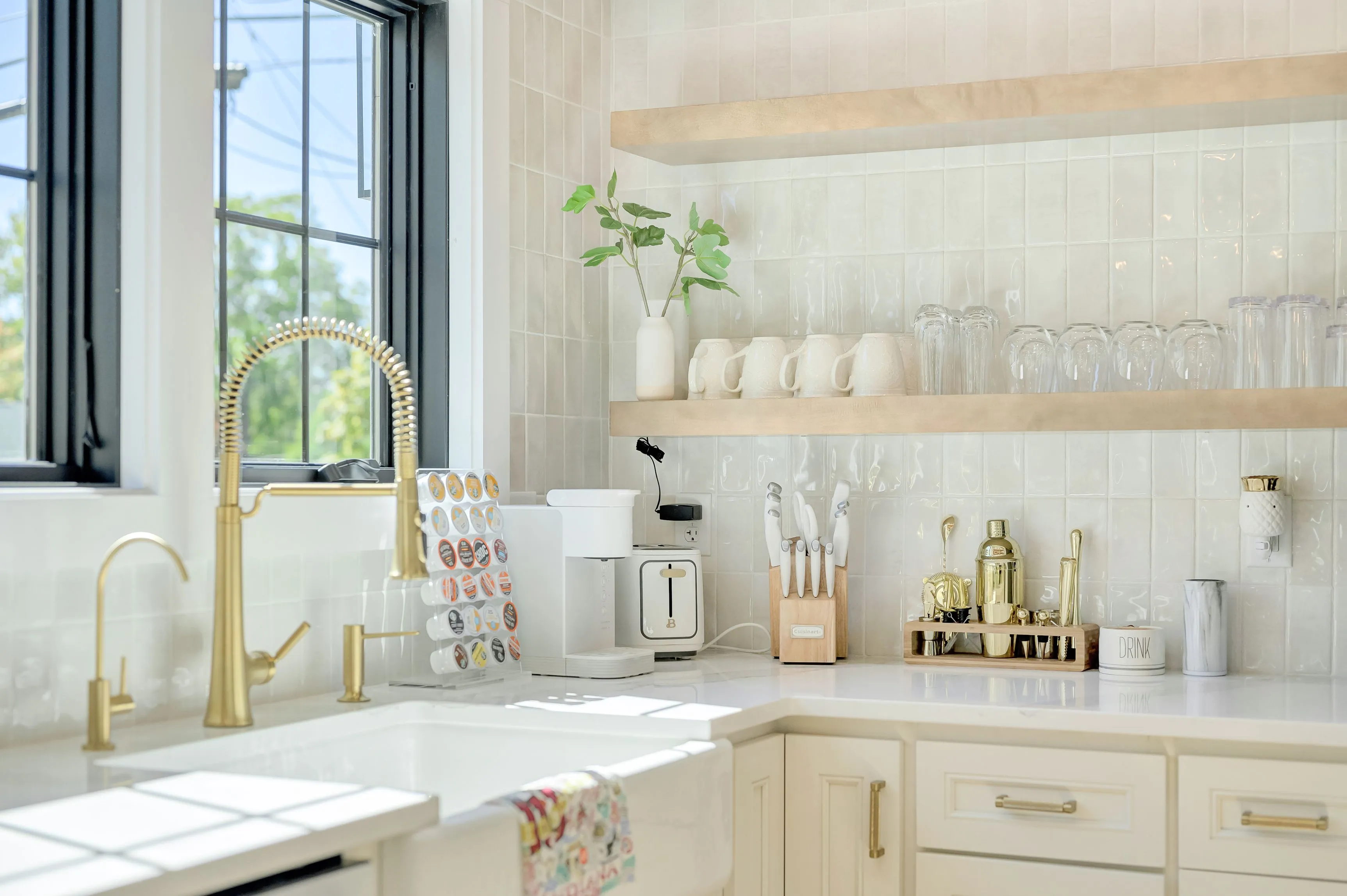 Bright modern kitchen interior with white cabinets, gold fixtures, and various utensils and appliances.