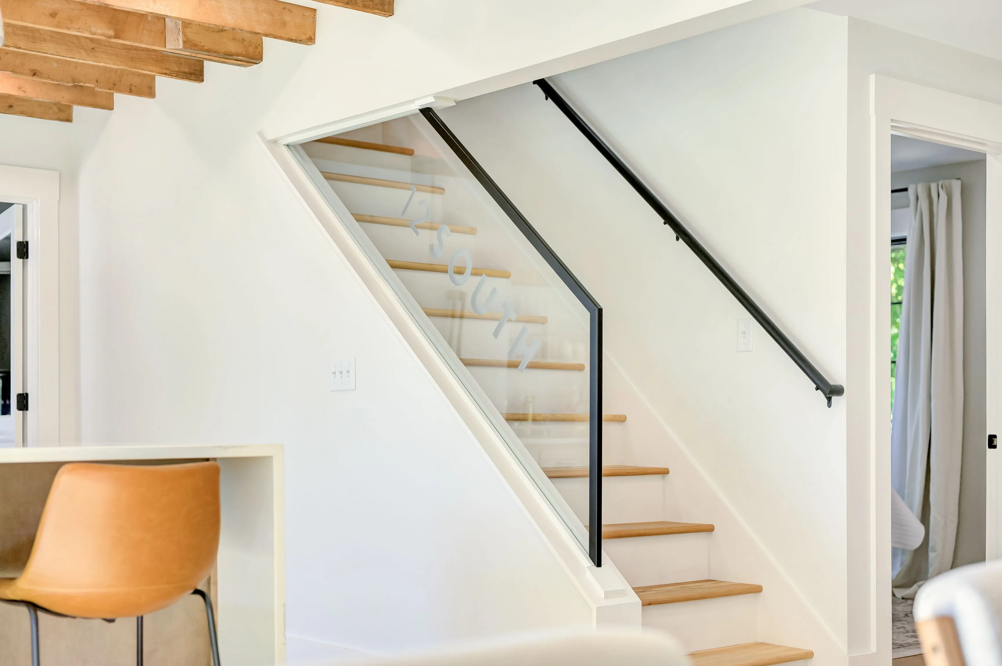 Modern staircase with wooden steps and black metal railing in a bright home interior with white walls and exposed wooden beams.