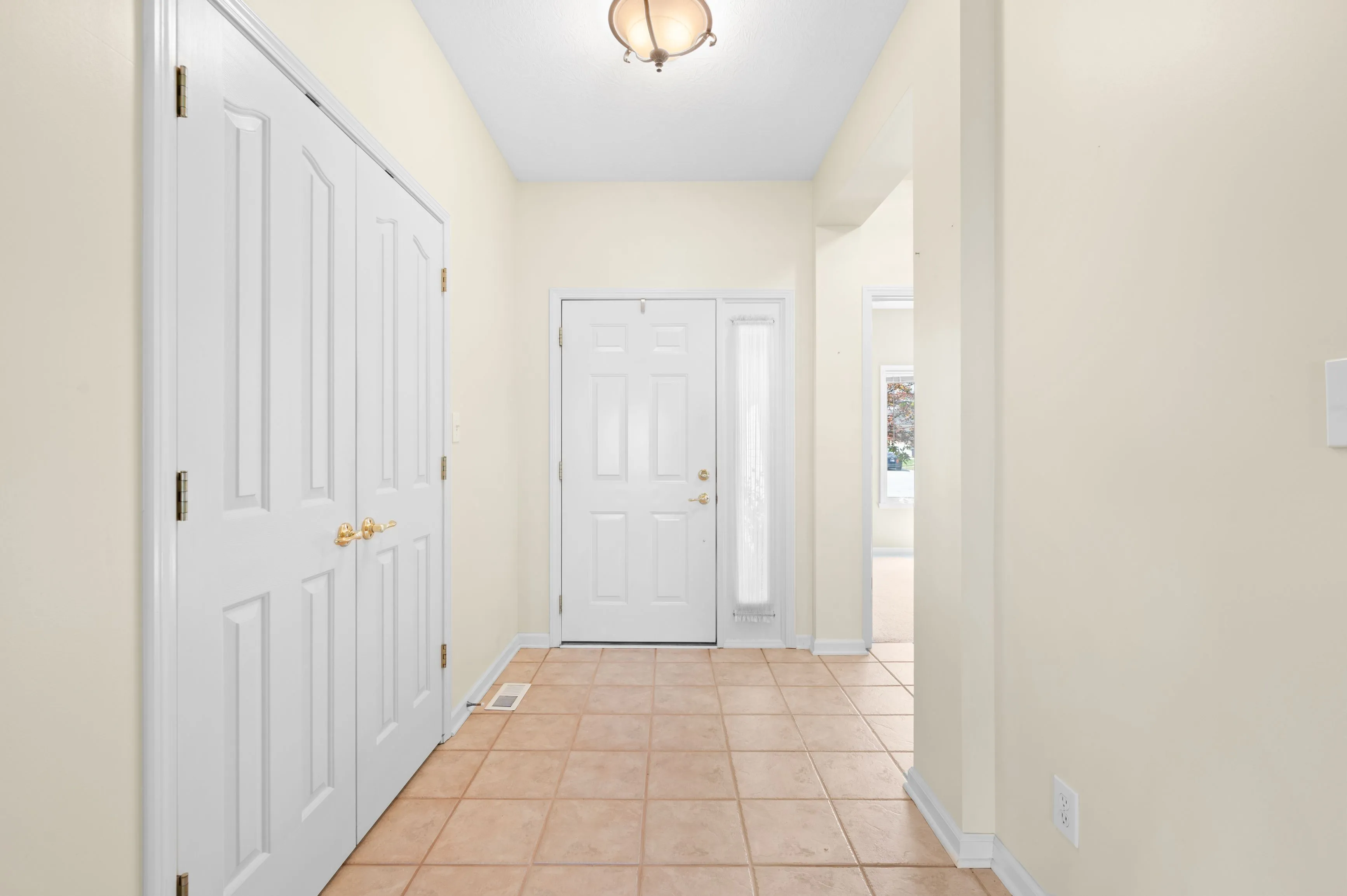 Bright entryway with tiled flooring, white doors, and a ceiling light fixture.
