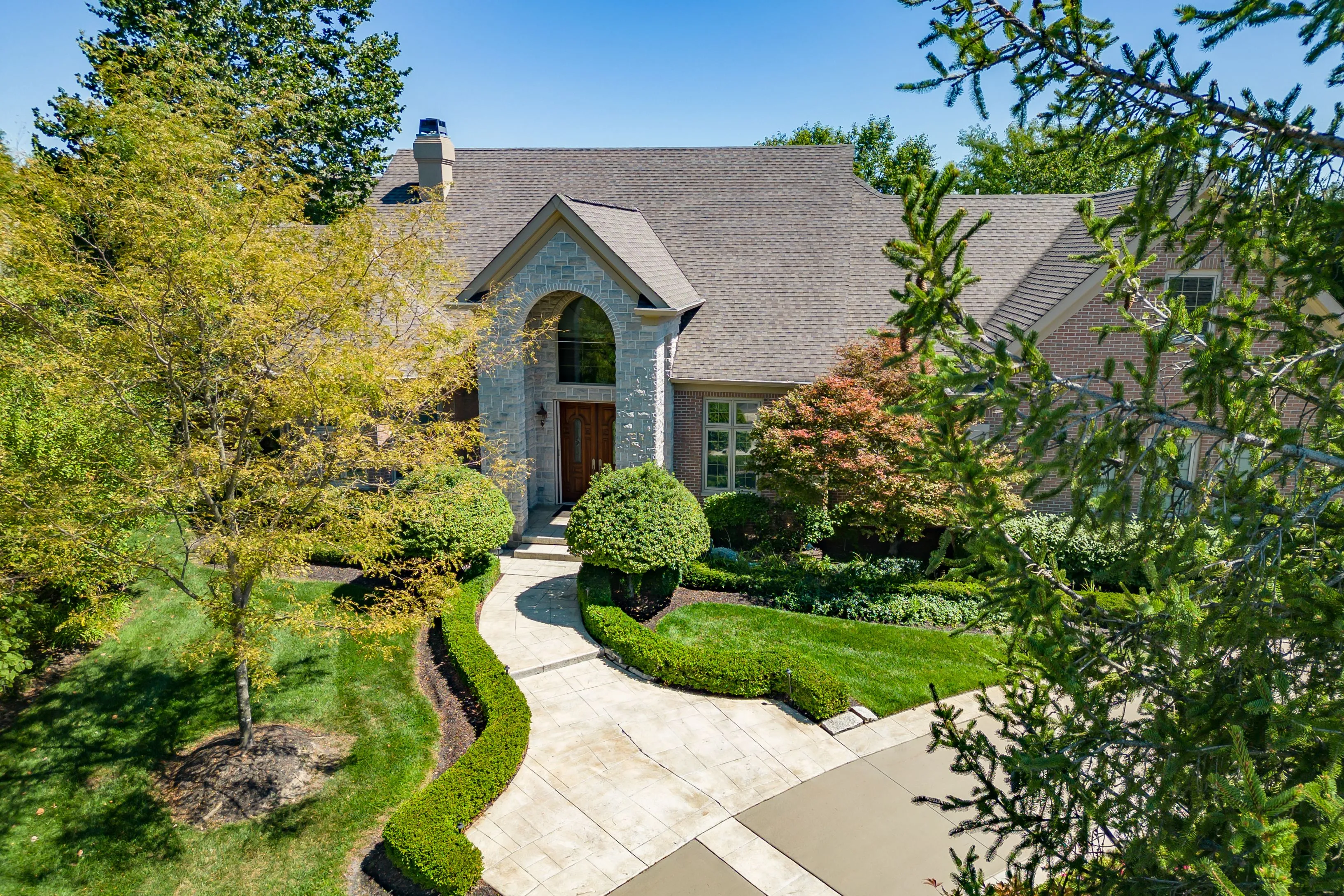 Two-story suburban house with a landscaped front yard and a stone pathway leading to an arched front entrance on a sunny day.