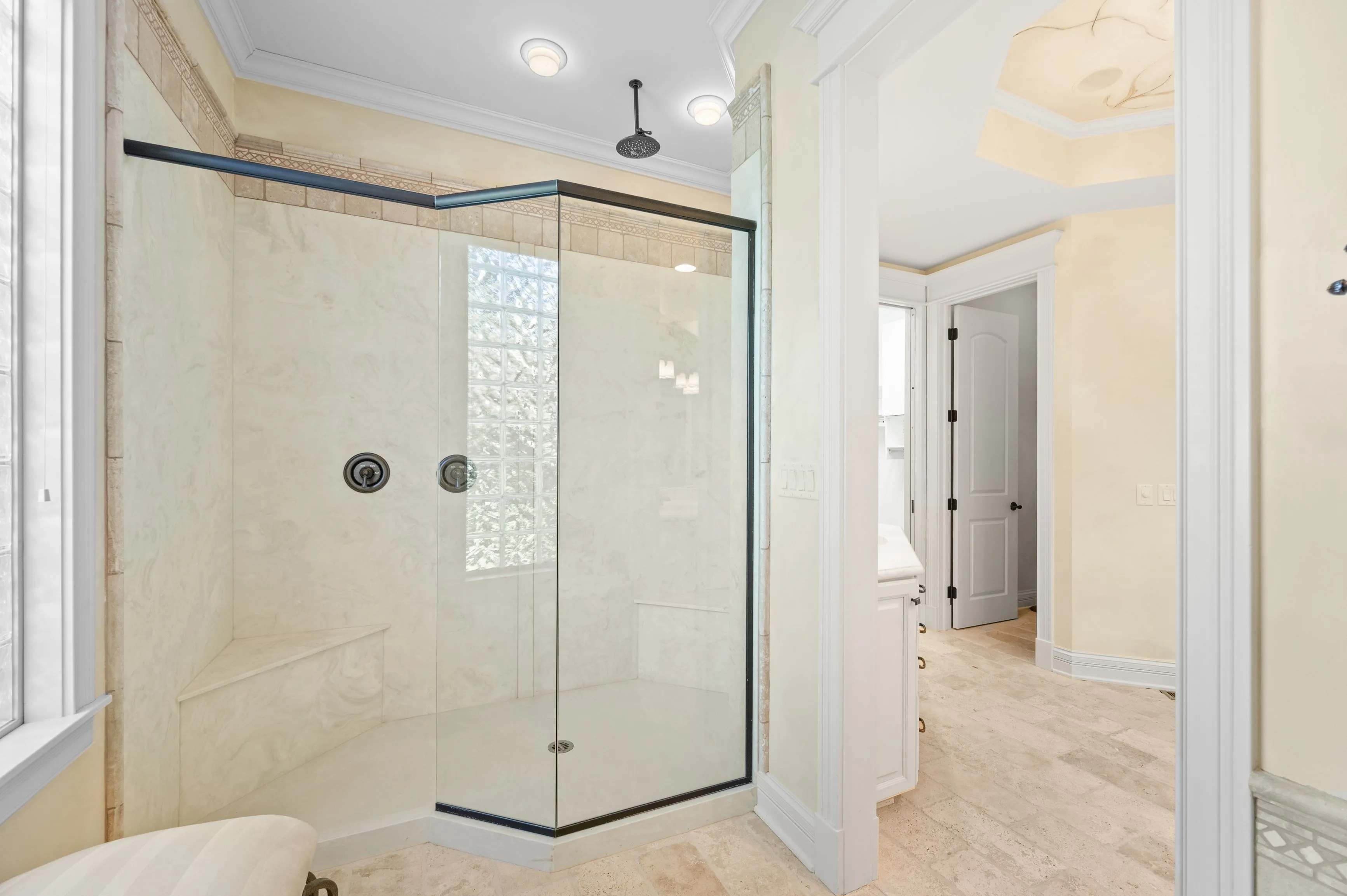 Elegant bathroom interior featuring a glass-enclosed shower with marble walls, seen through an open door with a view of a bedroom entrance in the background.