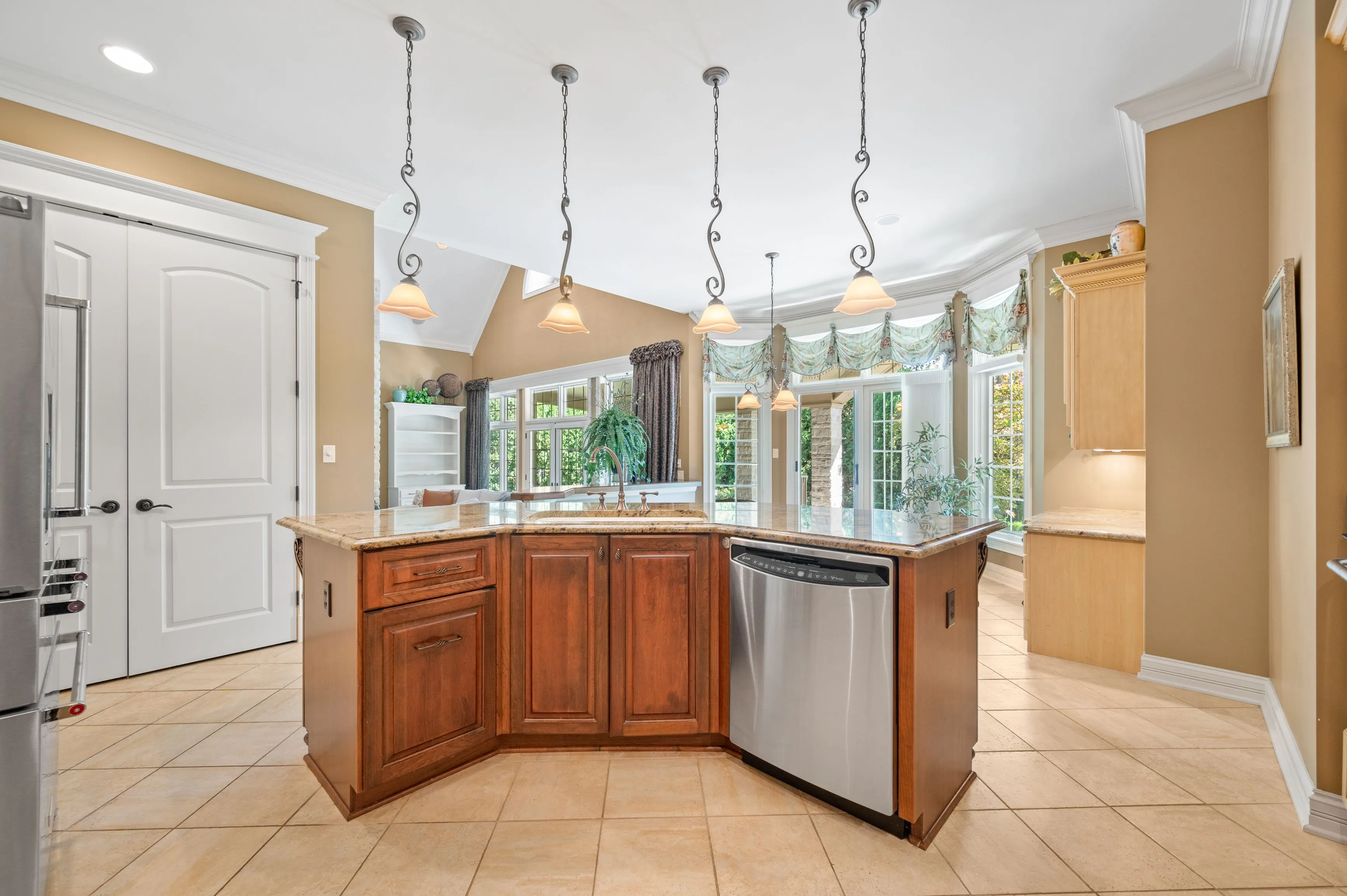 Bright and airy kitchen interior with wooden cabinets, granite countertops, stainless steel appliances, hanging pendant lights, and large windows with garden view.