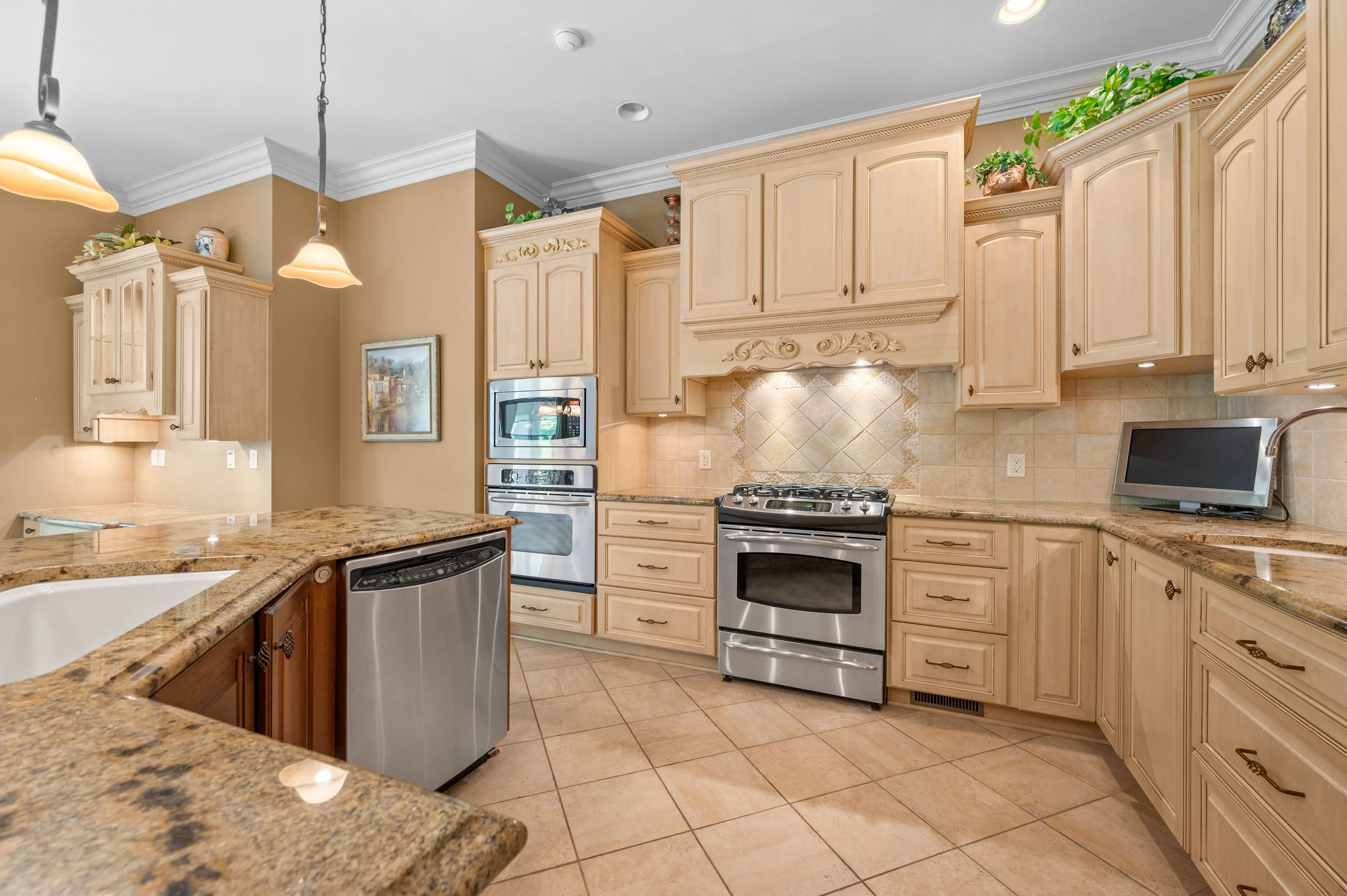 Spacious kitchen interior with beige cabinetry, granite countertops, stainless steel appliances, and pendant lighting.