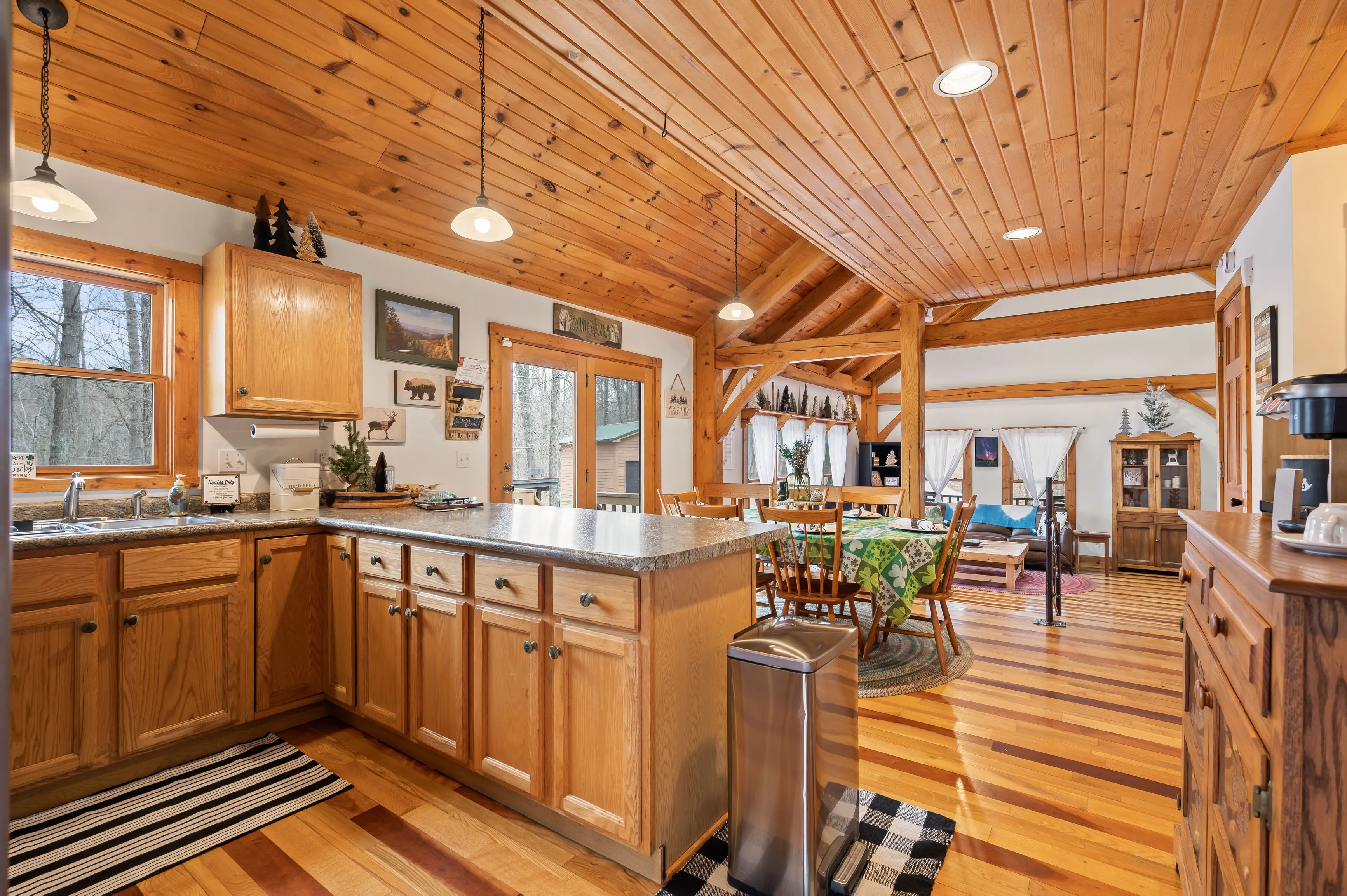 Spacious wooden cabin interior with a fully equipped kitchen, dining area, and a glimpse into the cozy living room with exposed beams and hardwood floors.