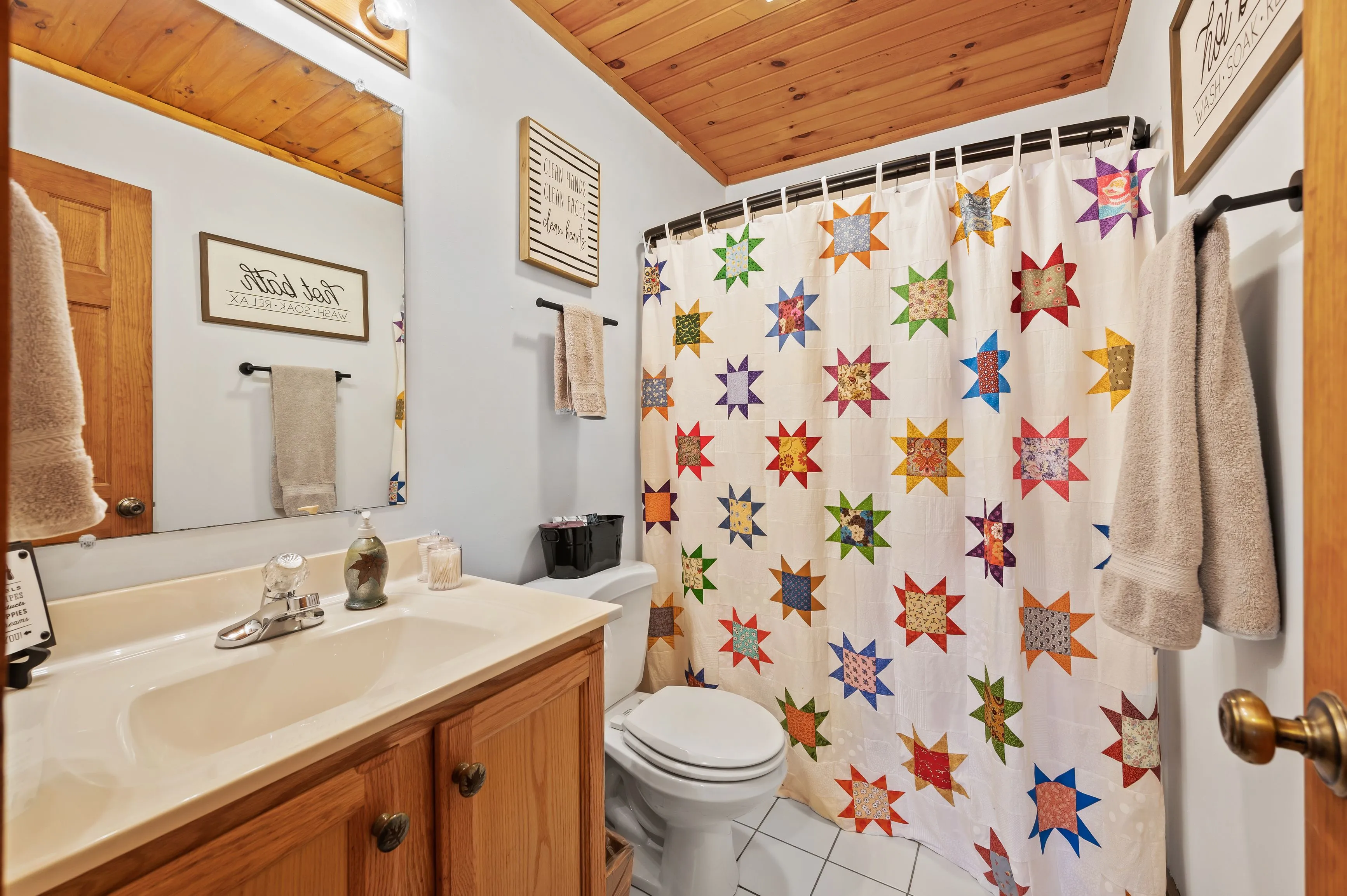 Cozy bathroom interior with wooden accents, a star-patterned shower curtain, and decorative wall art displaying sayings.