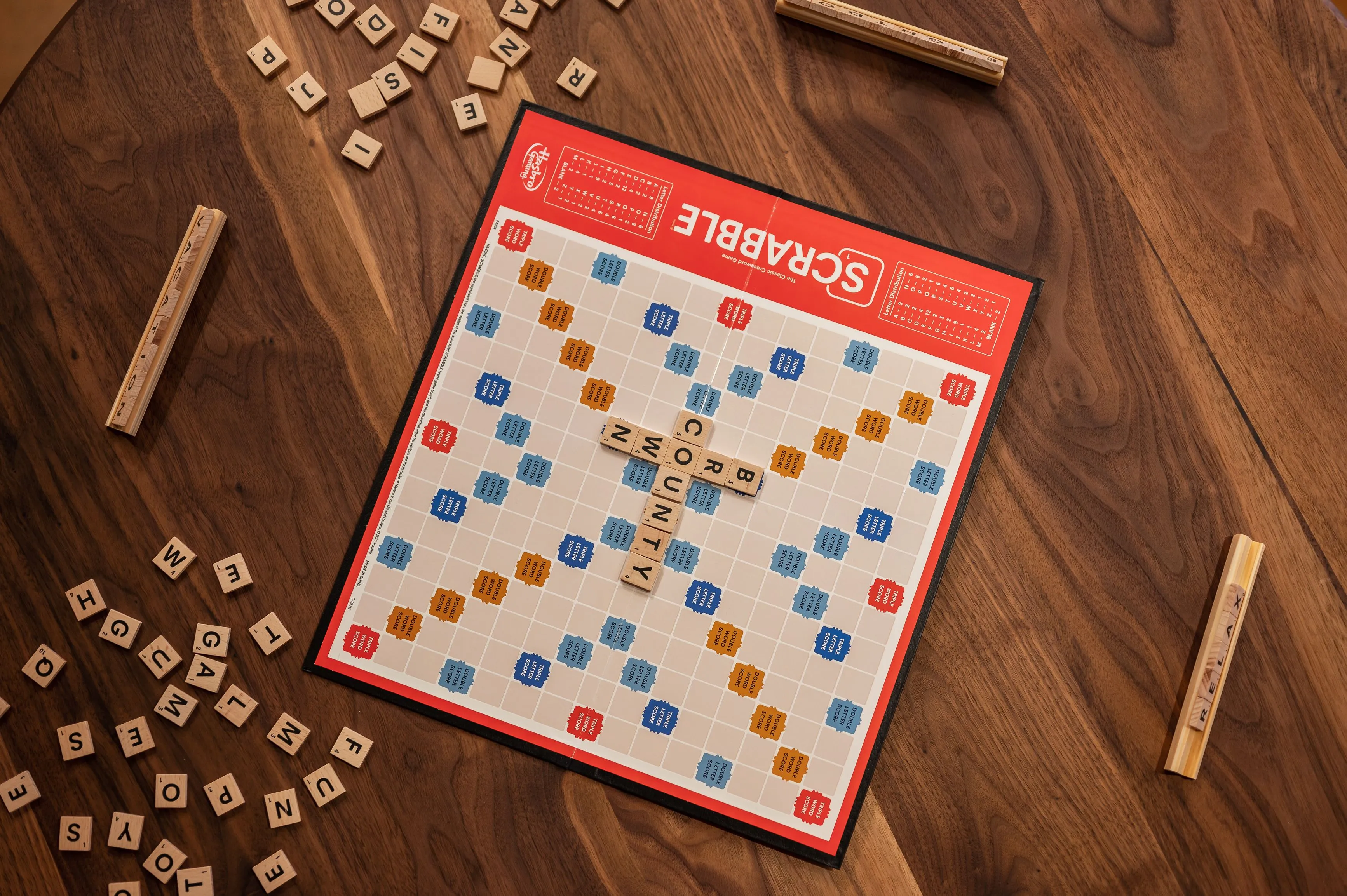 Scrabble board game on a wooden table with letter tiles scattered around and words 'COUNTY' on the board.
