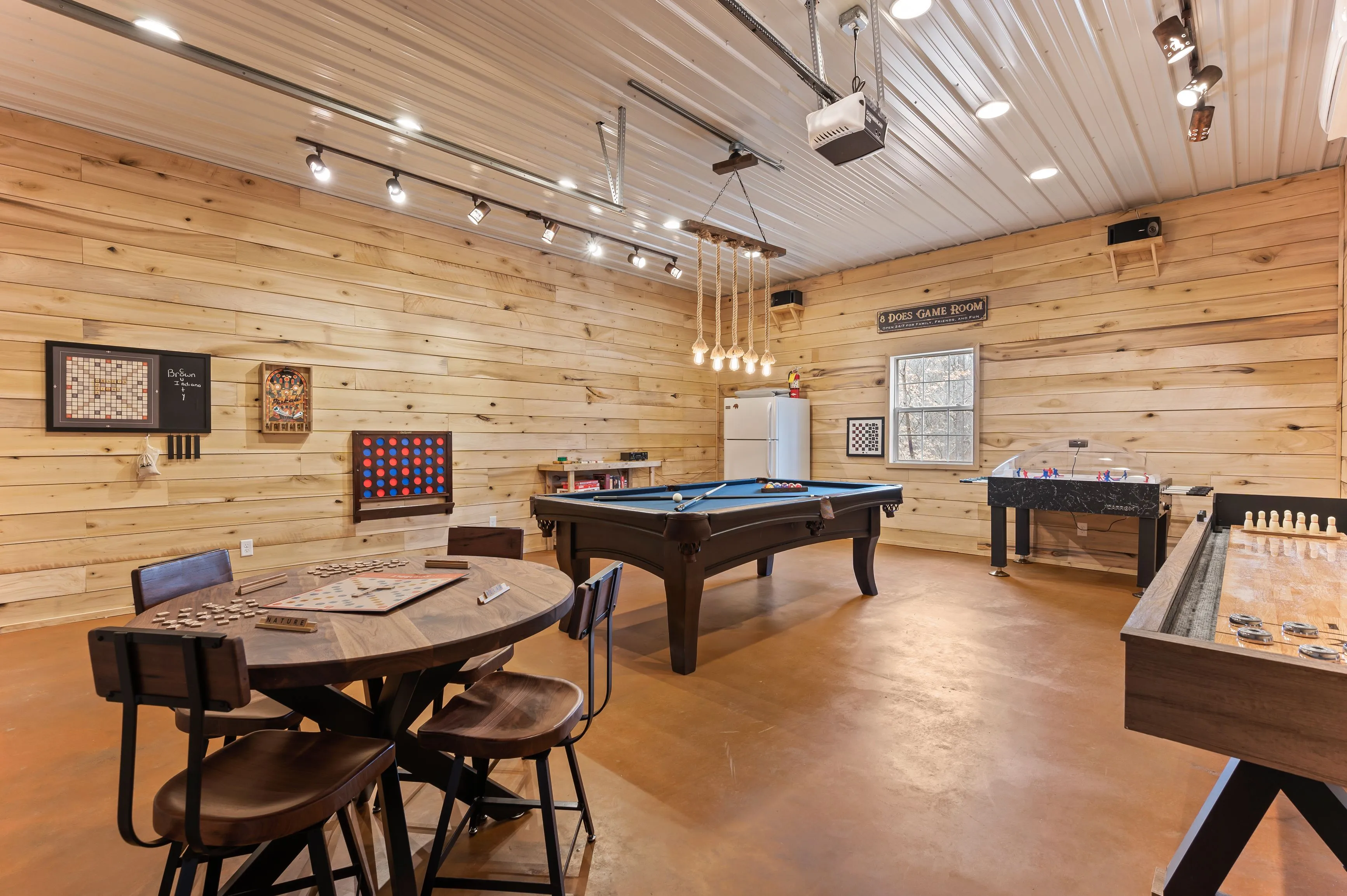 Spacious game room with wooden walls featuring a pool table, foosball, board games, and a unique hanging light fixture.