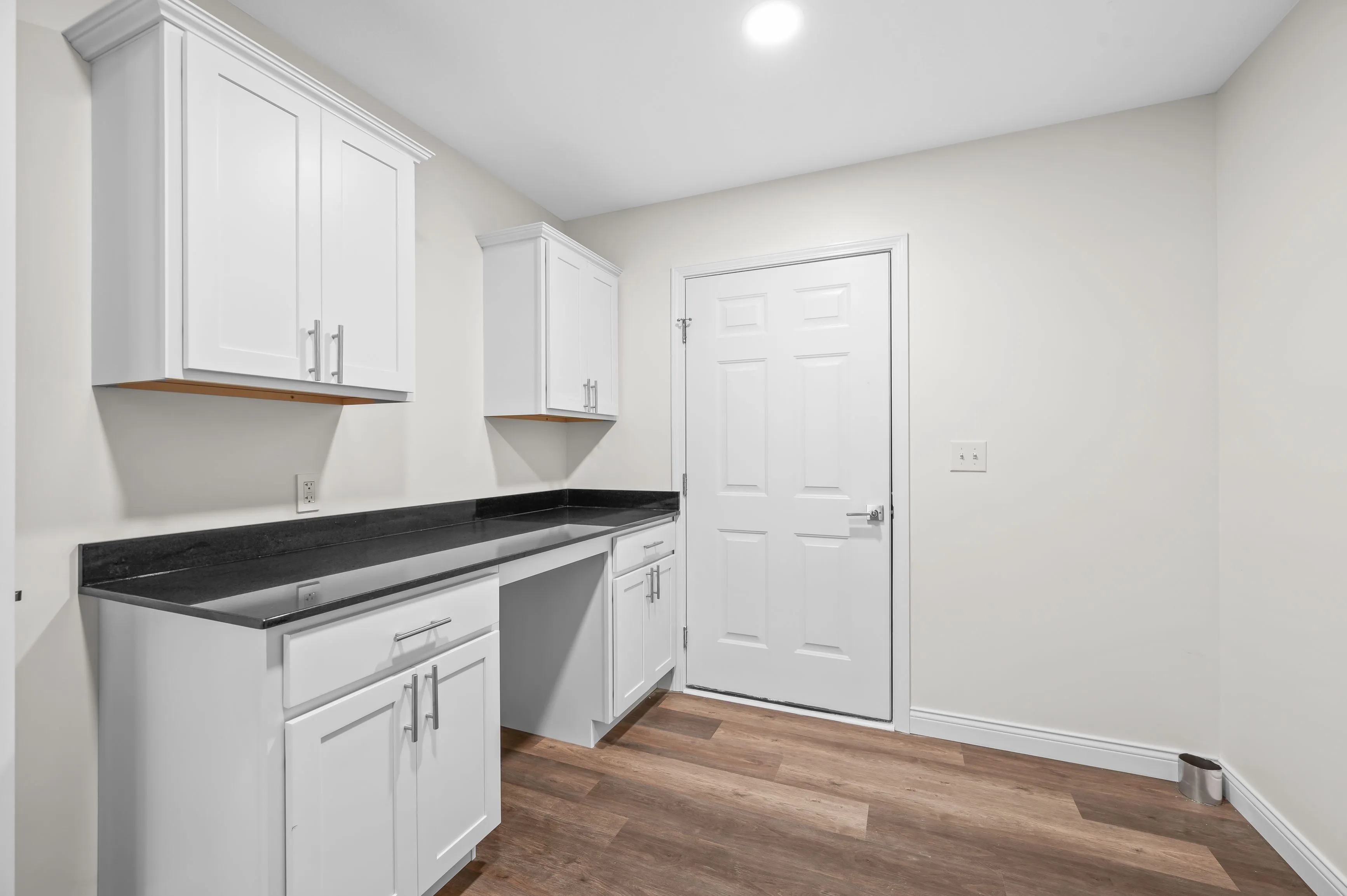 Modern kitchen corner with white cabinetry, dark countertops, and hardwood flooring.