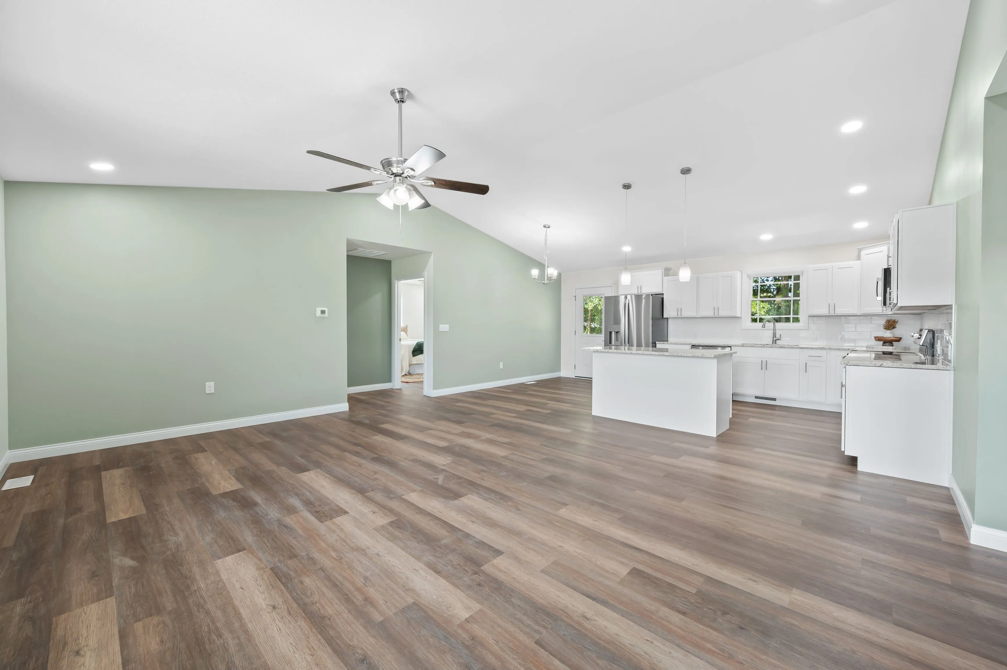 Spacious, modern kitchen with white cabinetry, stainless steel appliances, and a central island, leading into an open-plan living area with hardwood floors and pale green walls.
