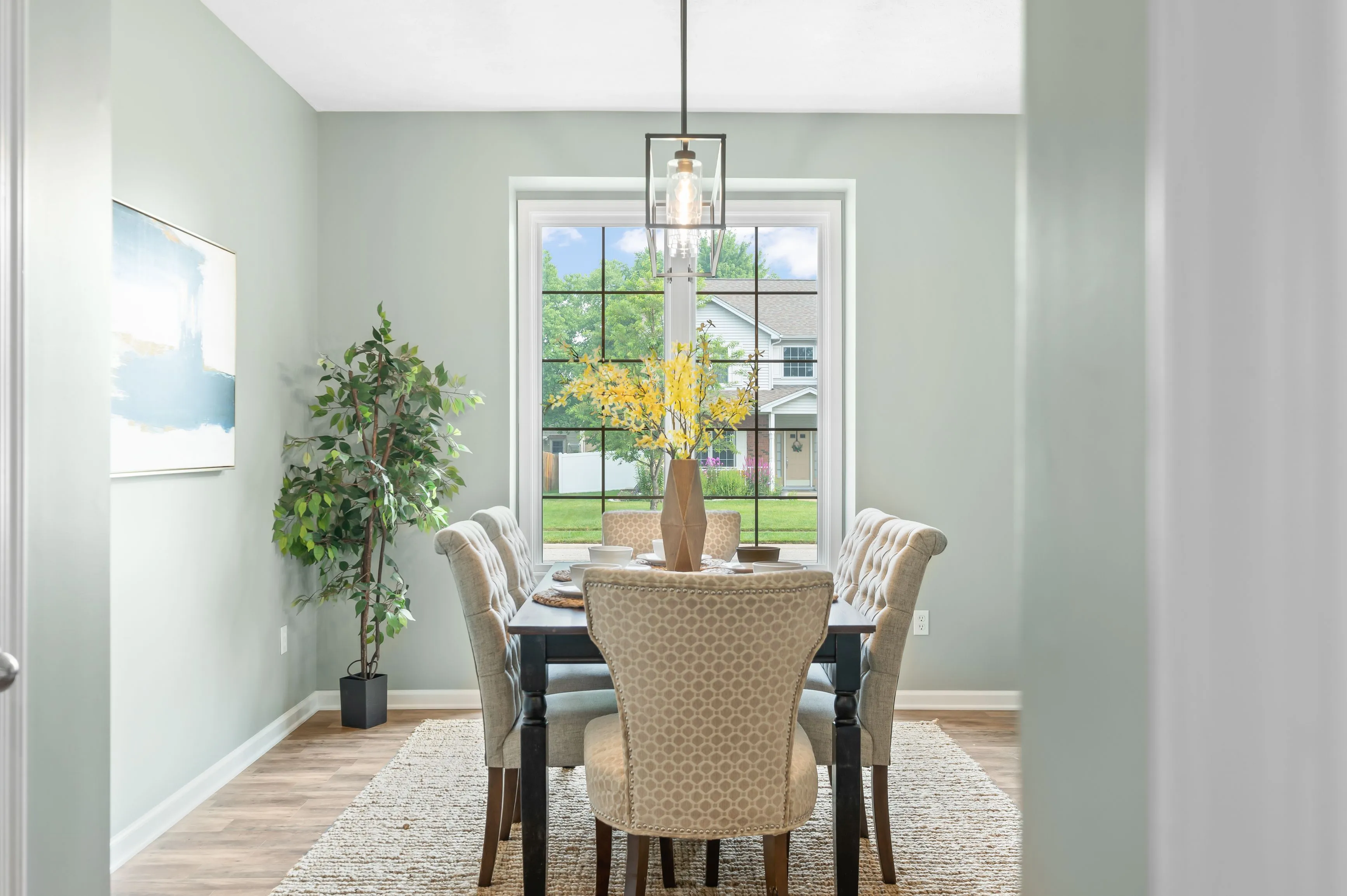Elegant dining room interior with a table set for four, pendant light, and a view of the backyard through large windows.