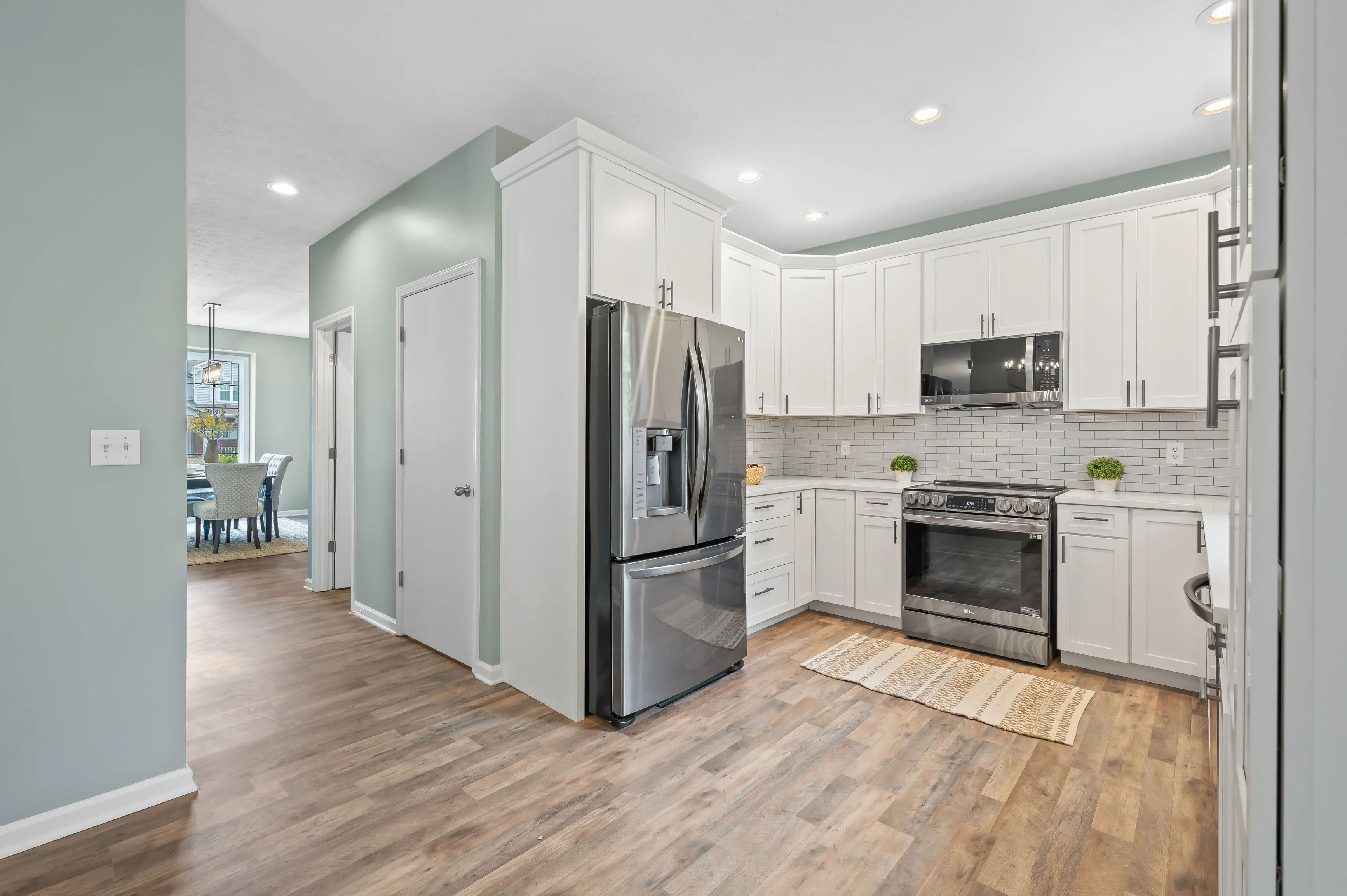 Modern kitchen interior with stainless steel appliances, white cabinets, and hardwood floors.