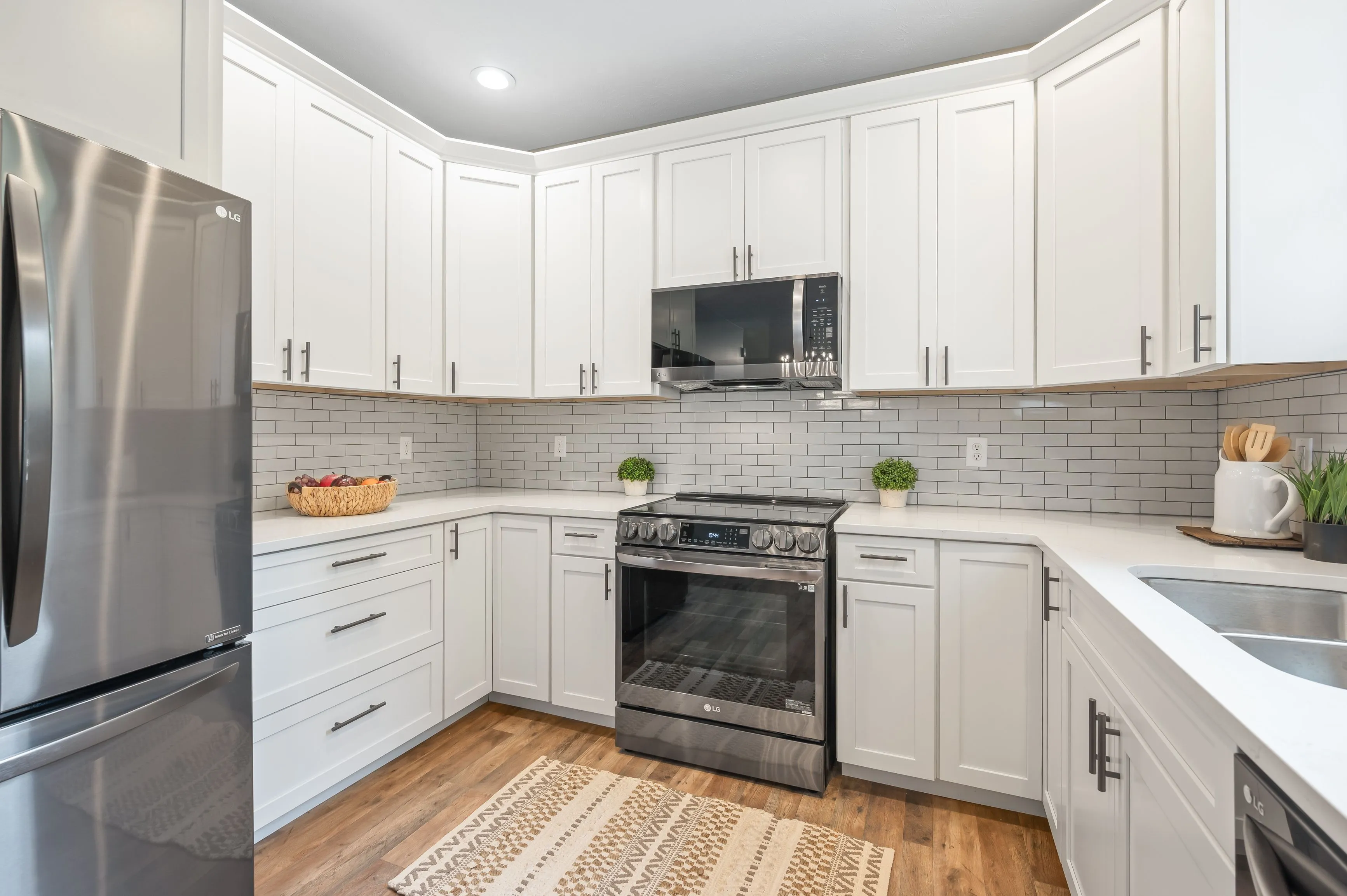 Modern kitchen interior with white cabinetry, stainless steel appliances, subway tile backsplash, and a patterned beige rug on wooden flooring.