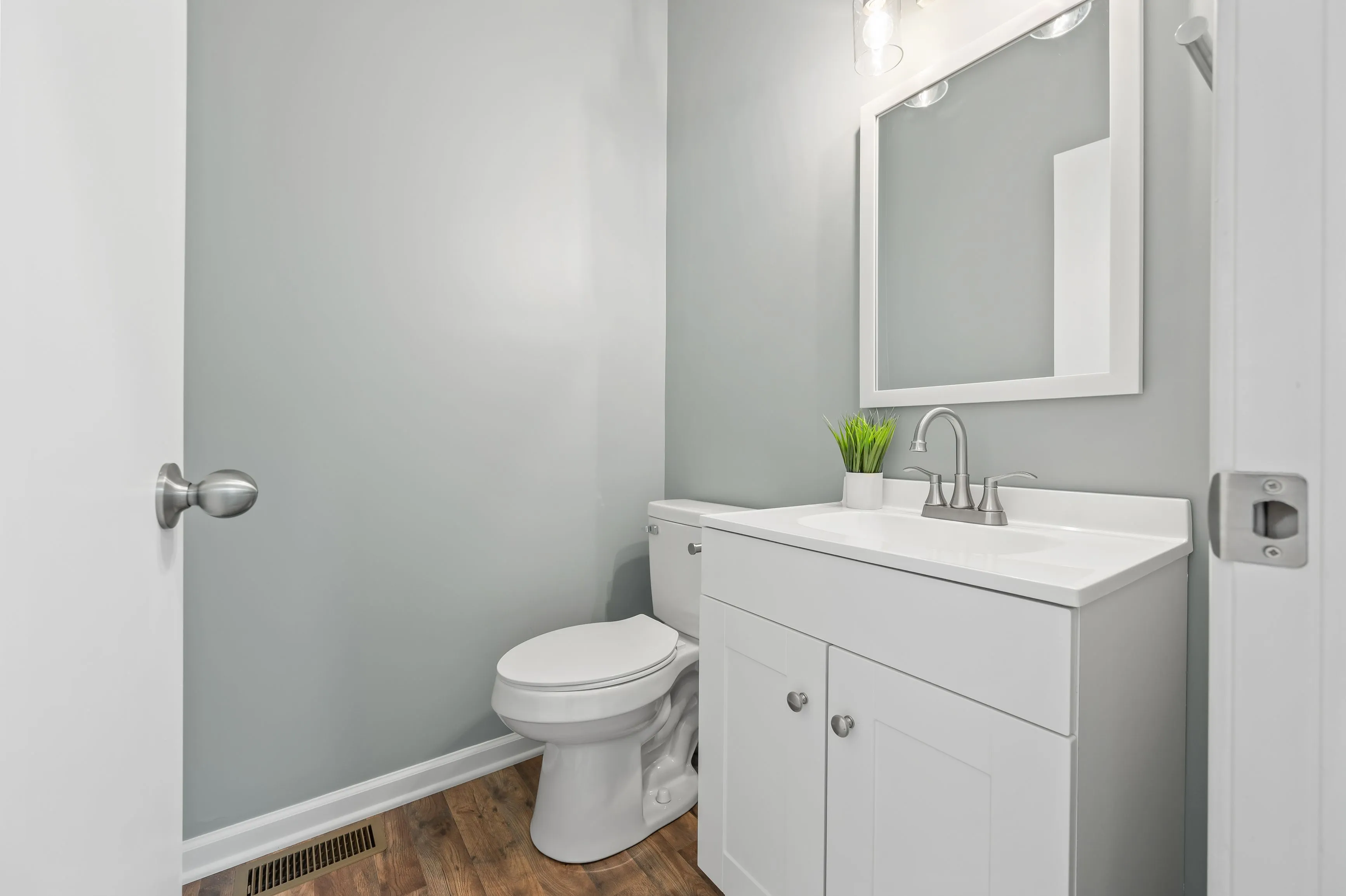 Modern bathroom with white vanity cabinet, sink, mirror, and toilet.