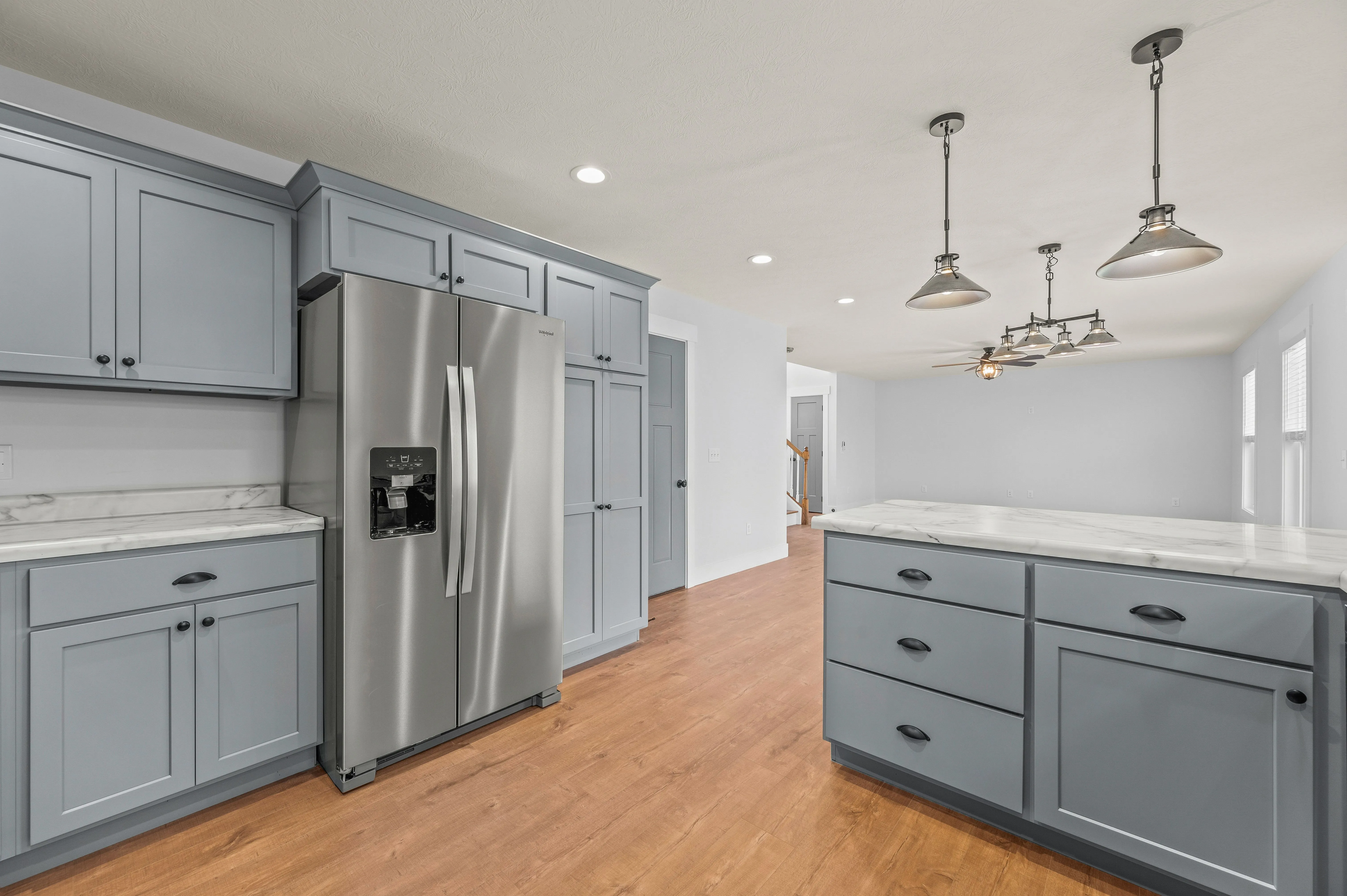 Modern kitchen interior with gray cabinets, stainless steel refrigerator, hardwood floors, and pendant lighting.