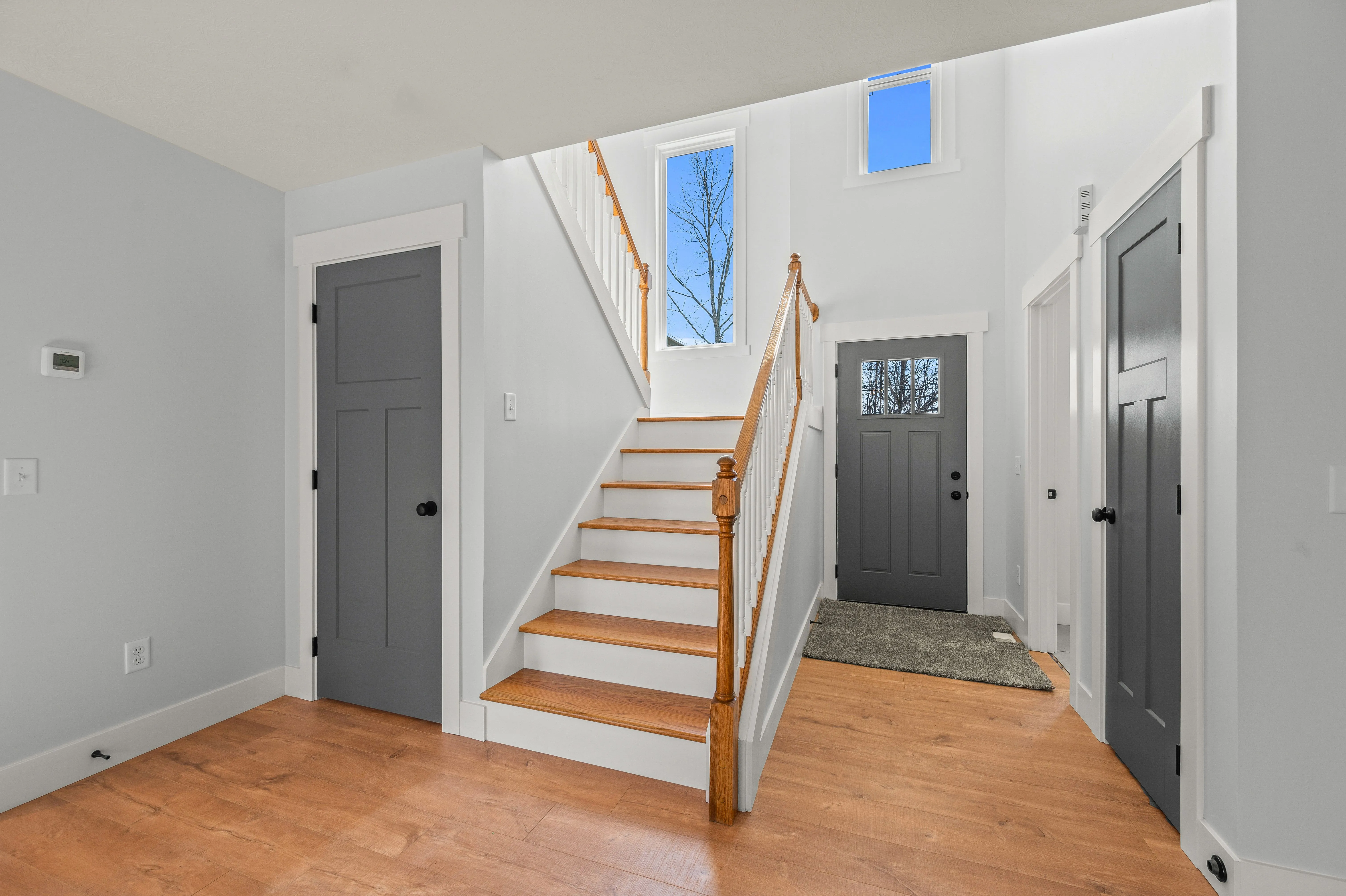 Bright entryway with wooden staircase, skylight, and multiple doors with dark hardware.