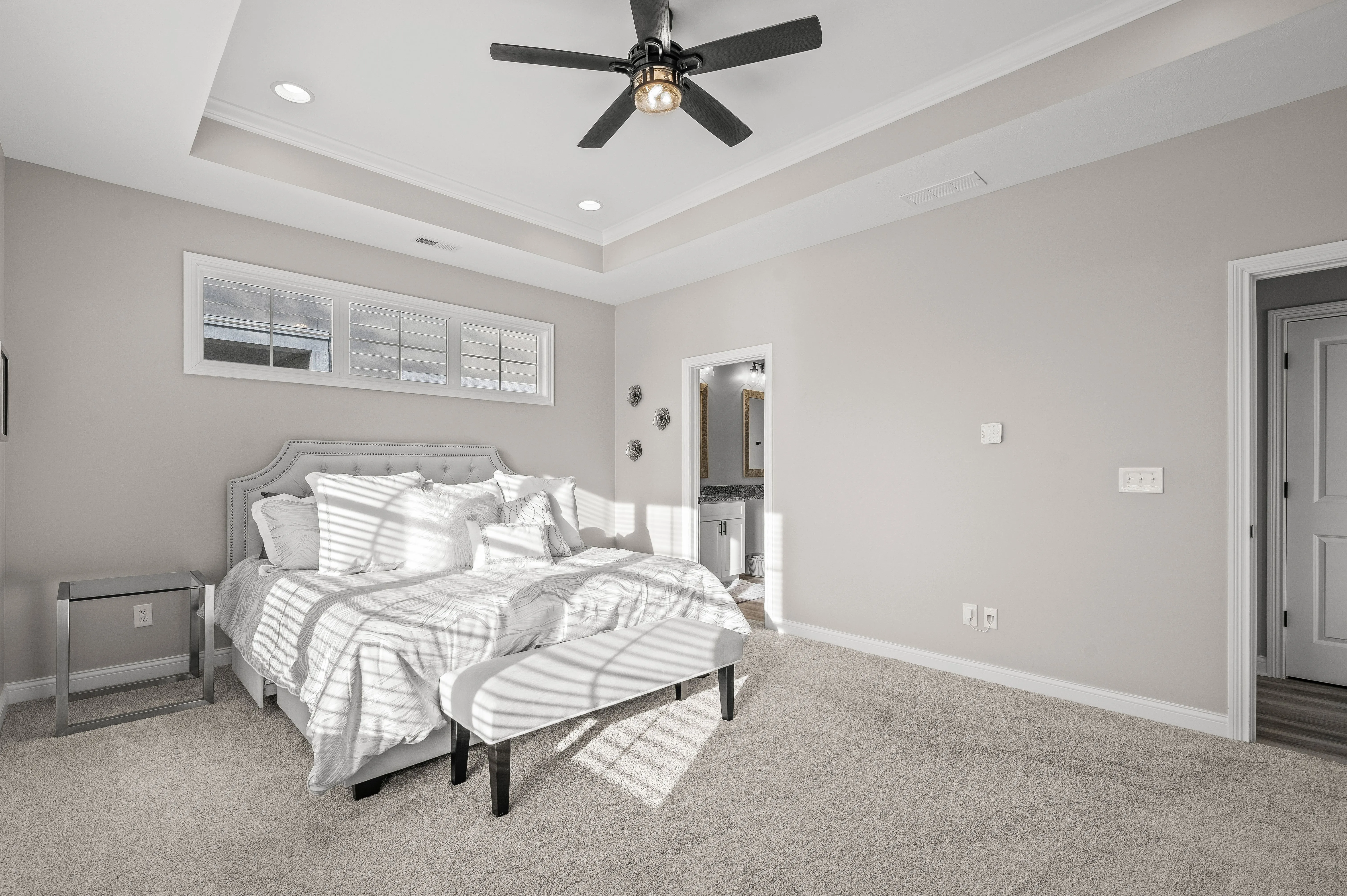 Bright and airy bedroom with a large bed, white and gray bedding, ceiling fan, and a glimpse into the en-suite bathroom.